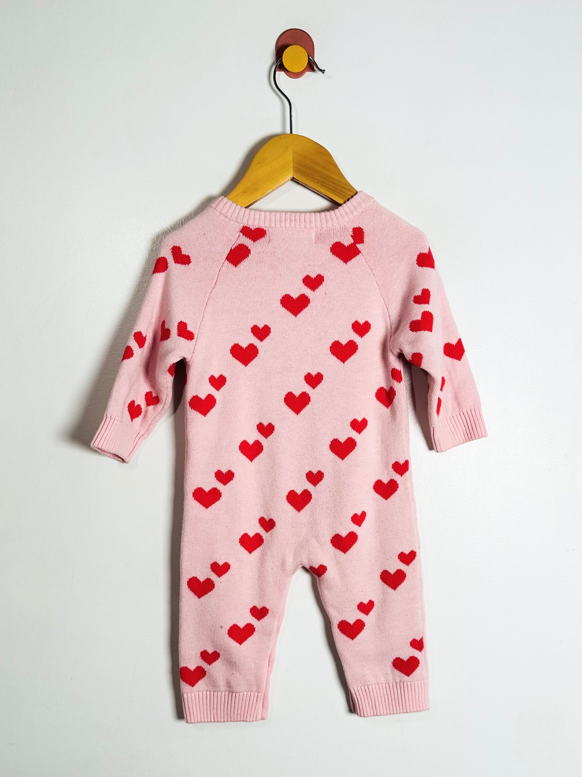 Pink baby romper with red heart patterns on a hanger against a white background