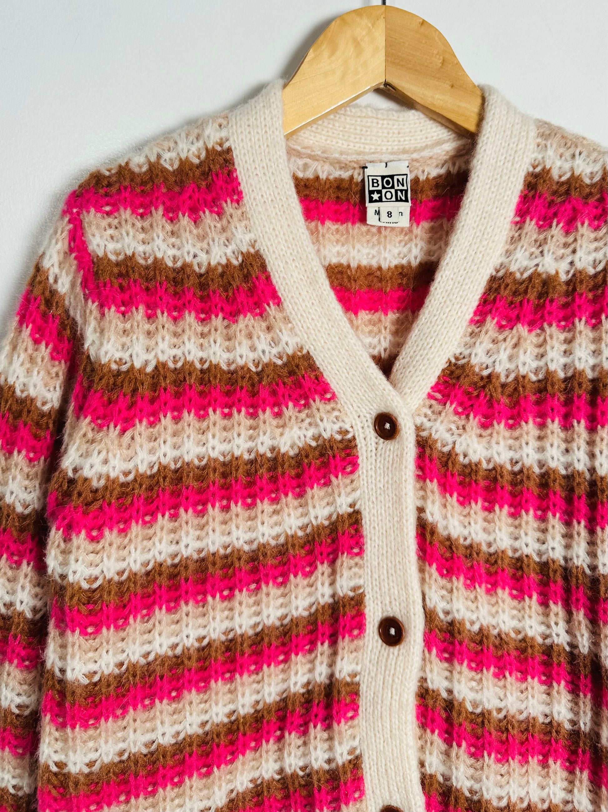 Striped cardigan with pink, brown, and beige pattern on a hanger against a white background