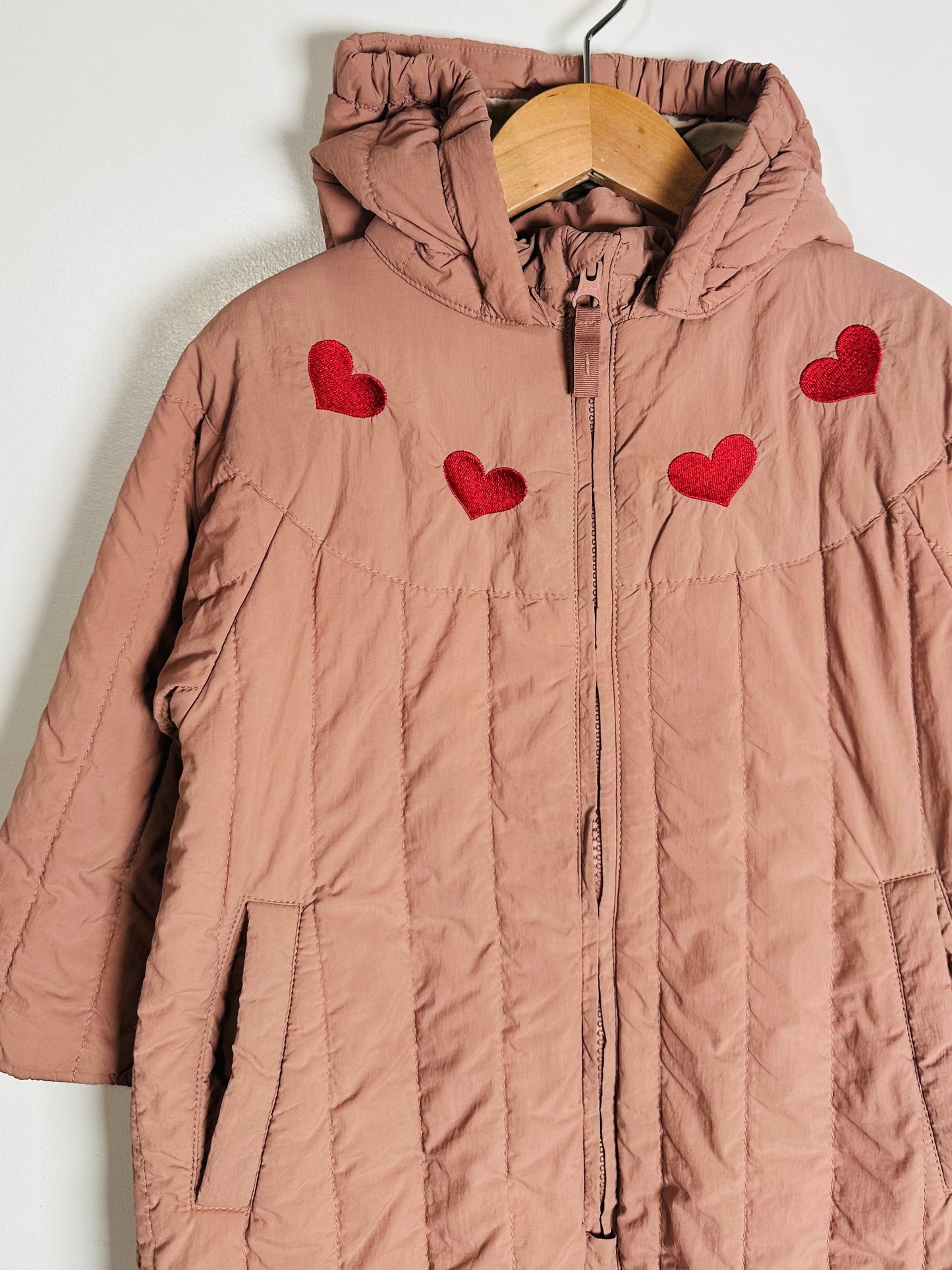 Pink quilted jacket with red heart designs on a white background