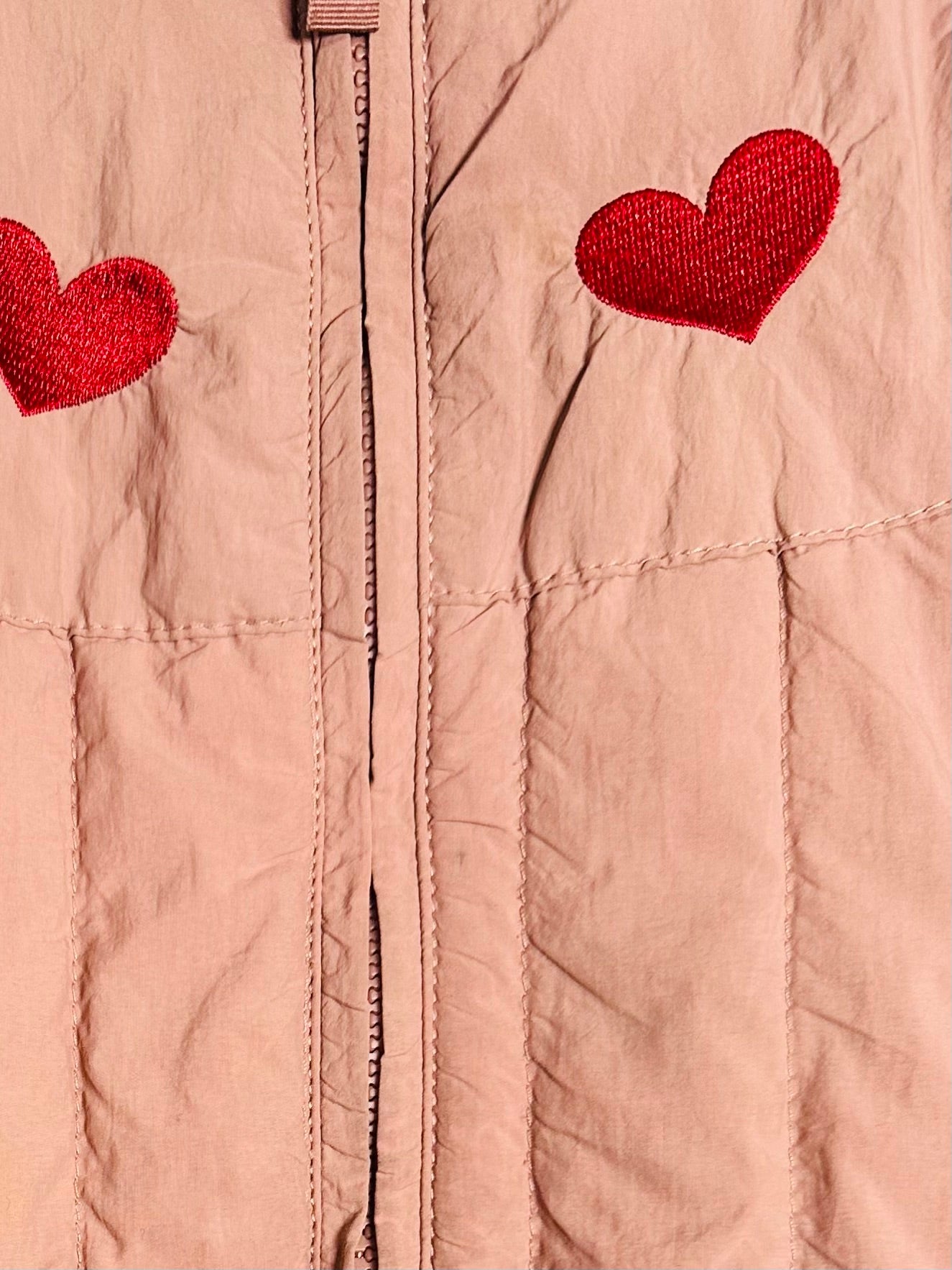 Close-up of a pink jacket with red heart patches on a beige background