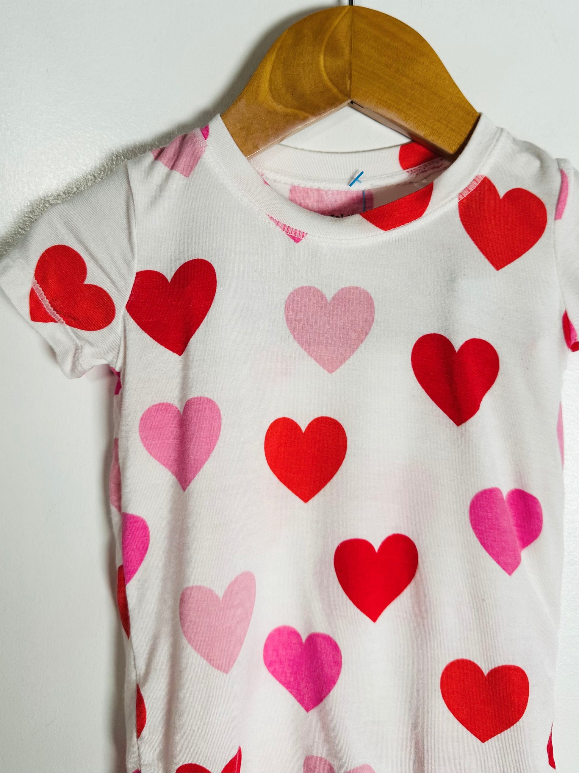 White t-shirt with red and pink heart patterns on a wooden hanger against a white background