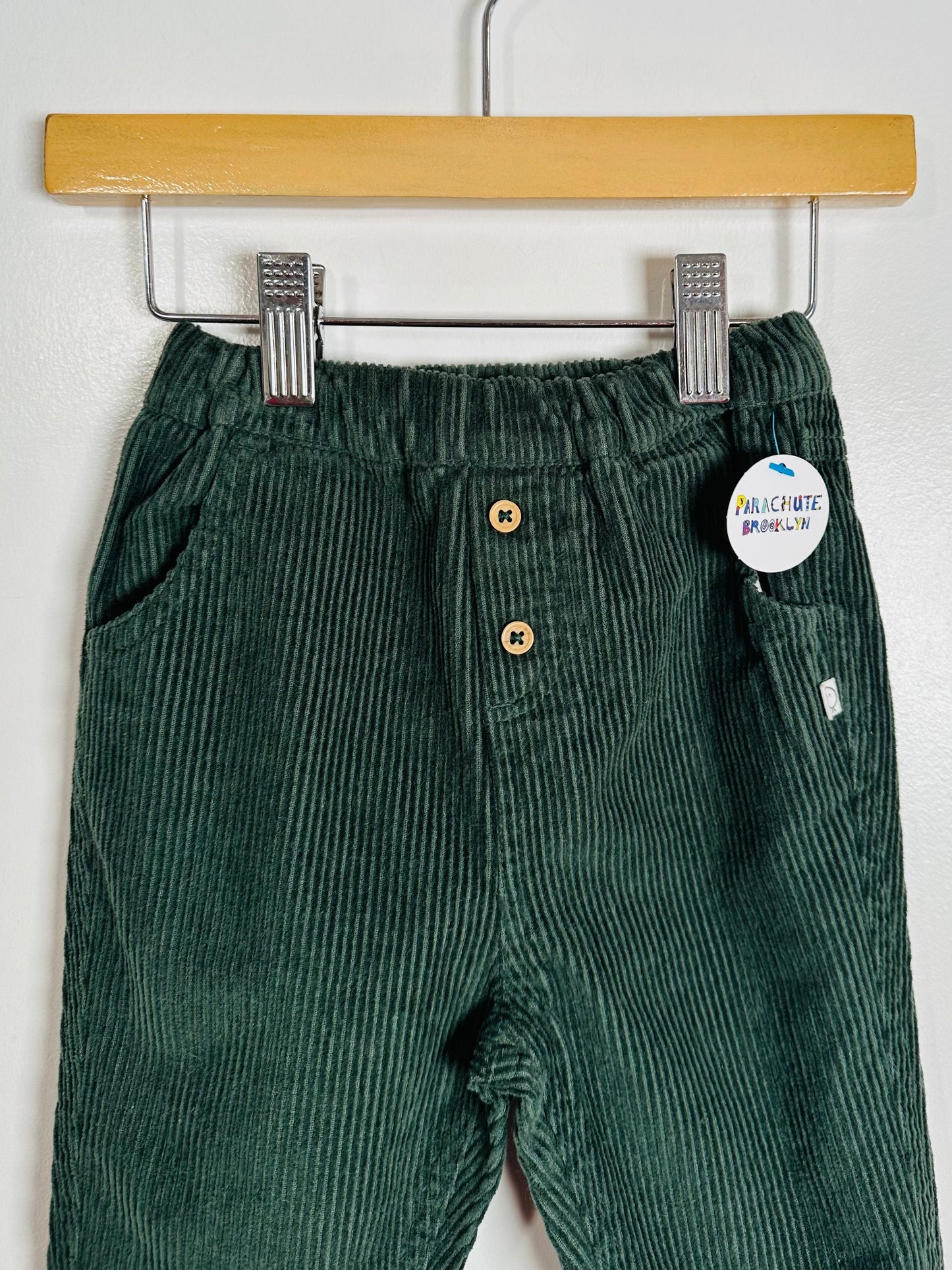 Green corduroy pants on a hanger with a visible brand tag.