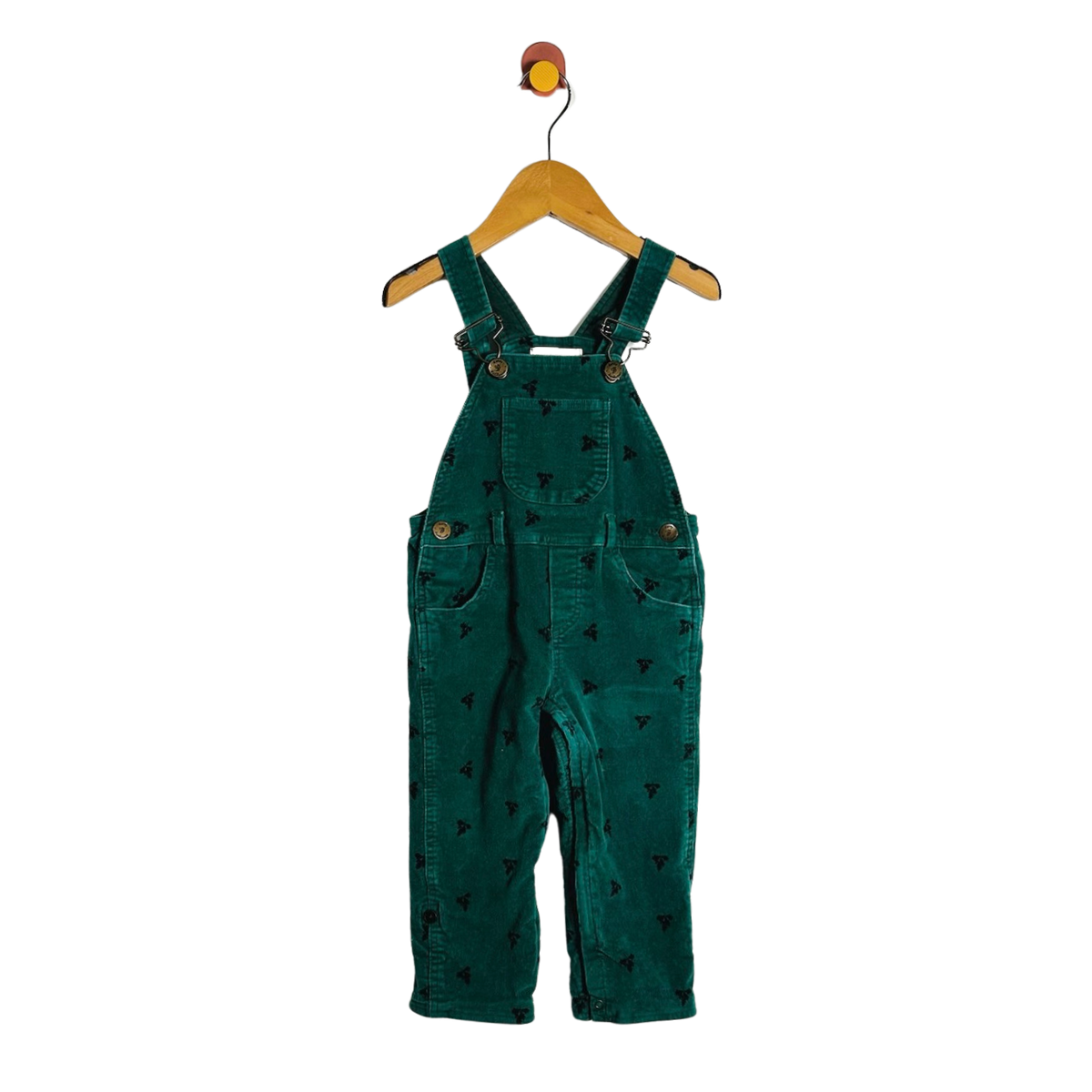 A pair of toddler green corduroy bib overalls with a small black pattern, hanging on a wooden hanger against a white background.