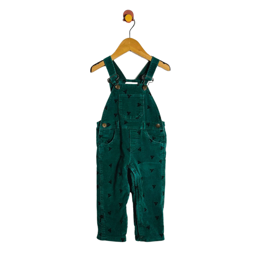 A pair of toddler green corduroy bib overalls with a small black pattern, hanging on a wooden hanger against a white background.