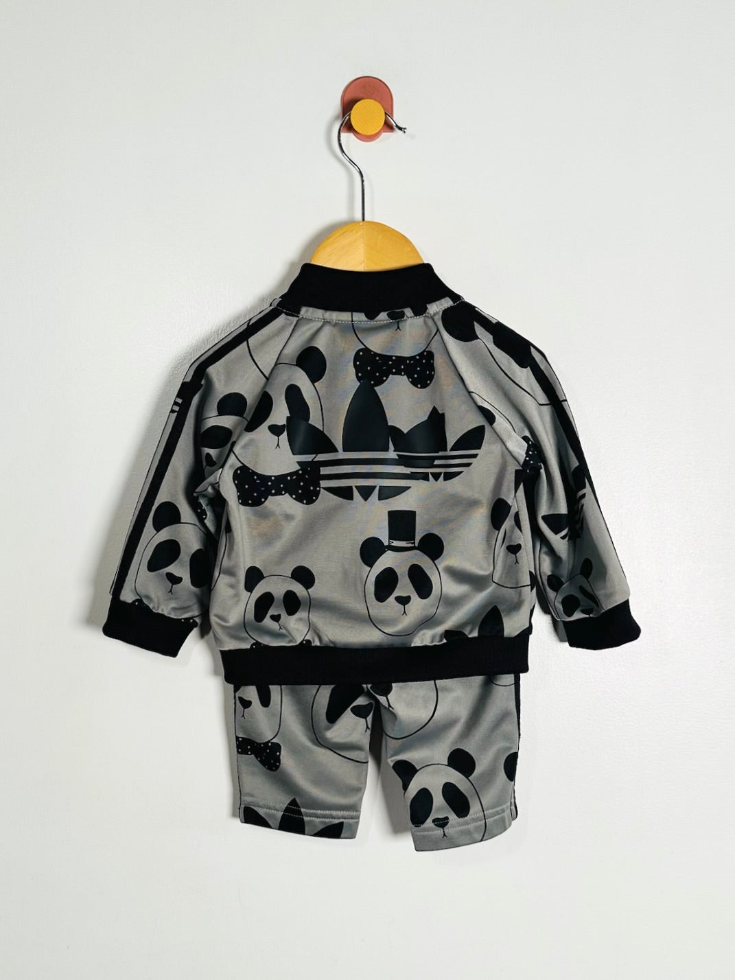 A toddler's two-piece tracksuit set consisting of a zip-up jacket and matching shorts, featuring a gray satin-like fabric with a black panda print and black ribbed trim, hanging on a wooden hanger against a plain white wall.