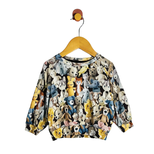 A long-sleeve crewneck sweatshirt for toddlers, featuring an all-over colorful print of teddy bears, dogs, cats, and other cartoon animals. The sweatshirt is displayed on a wooden hanger against a solid white background.