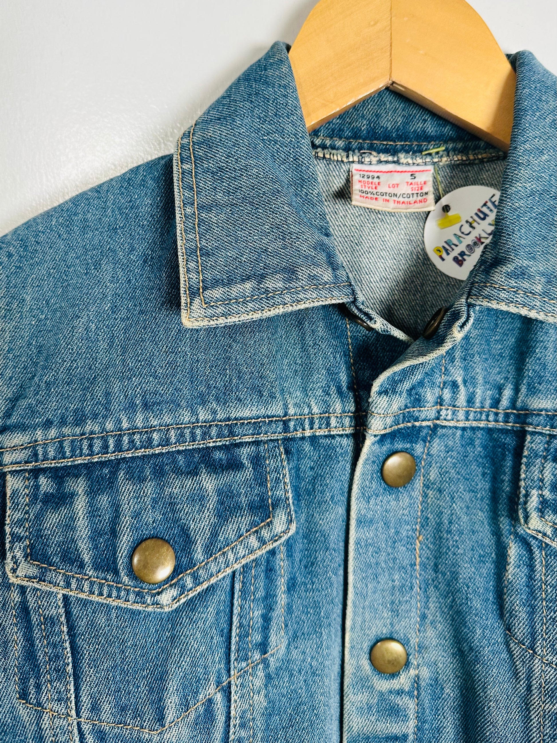 Close-up of a blue denim jacket with a brand label on a wooden hanger.