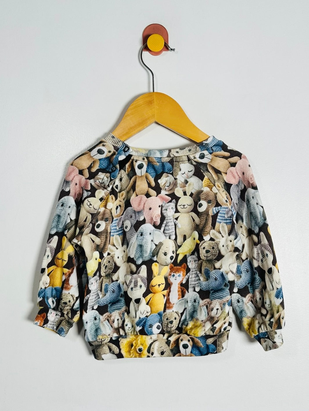 A long-sleeve crewneck sweatshirt featuring an all-over print of various cartoon teddy bears, hanging on a wooden hanger against a plain light gray wall.