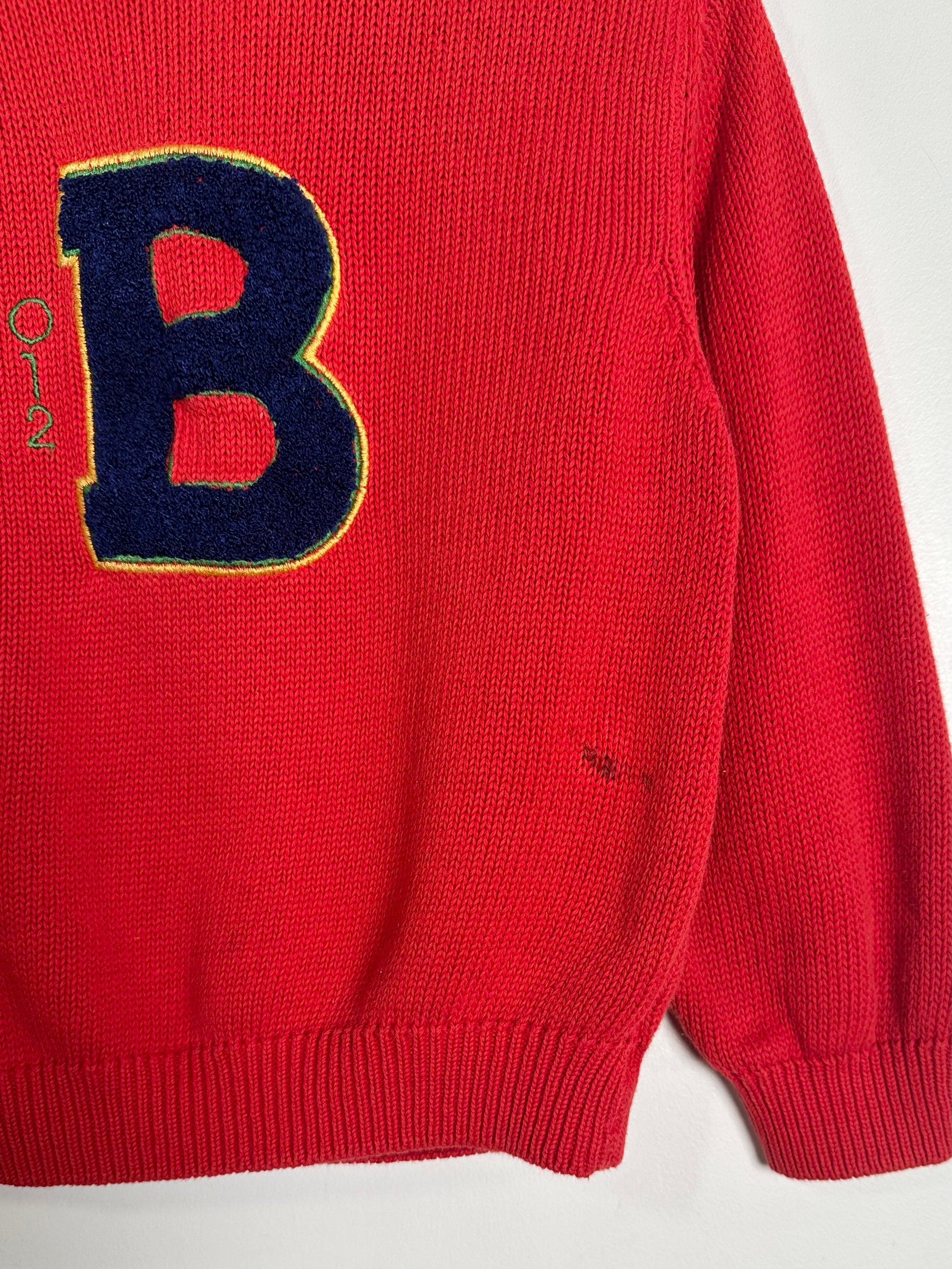 Red sweater with a large blue 'B' on a white background