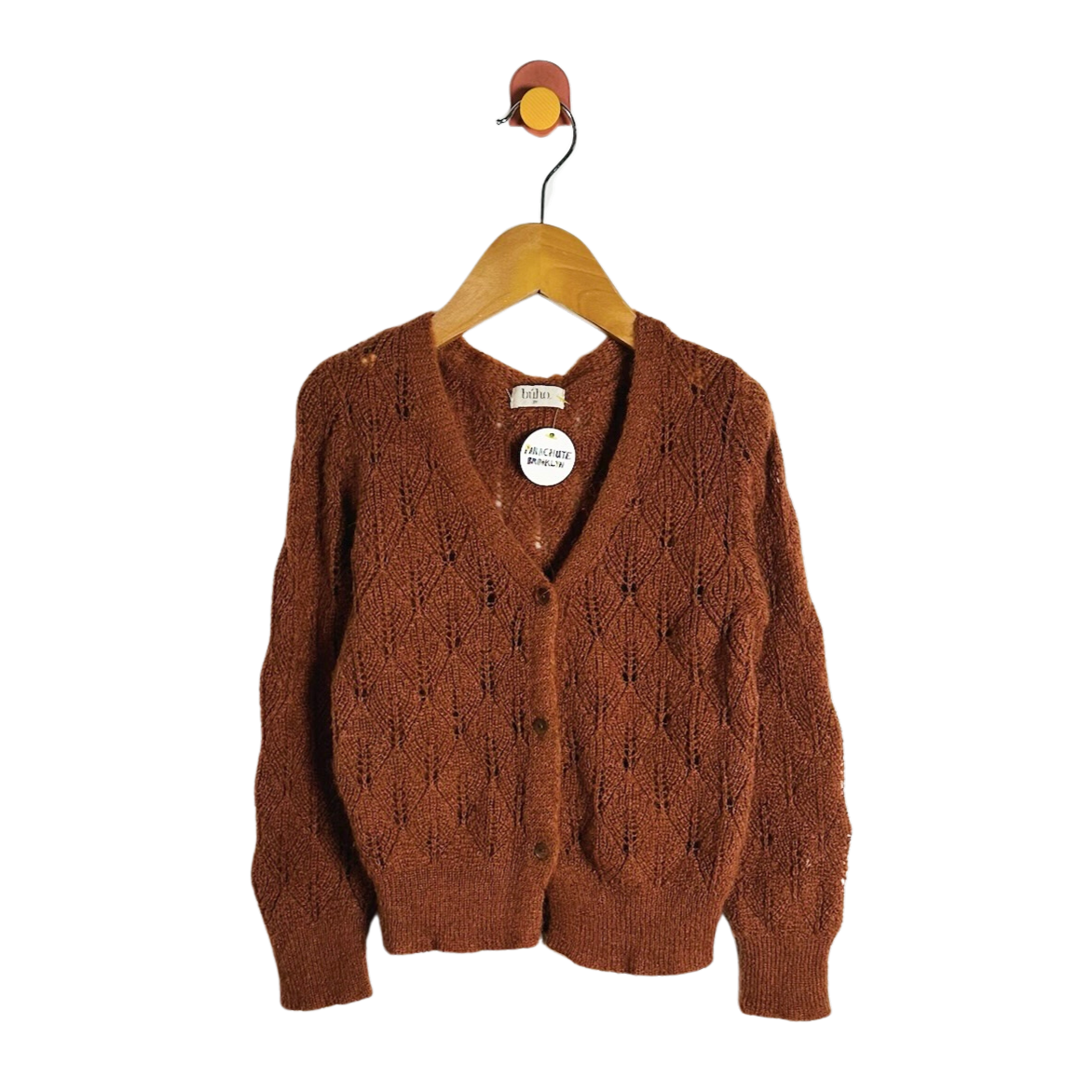 A rust-brown cable-knit cardigan sweater hanging on a wooden hanger against a plain white background.