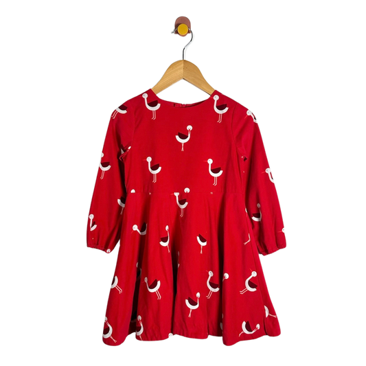 A red long-sleeve dress with a white and black bird pattern, hanging on a wooden hanger against a plain white background.