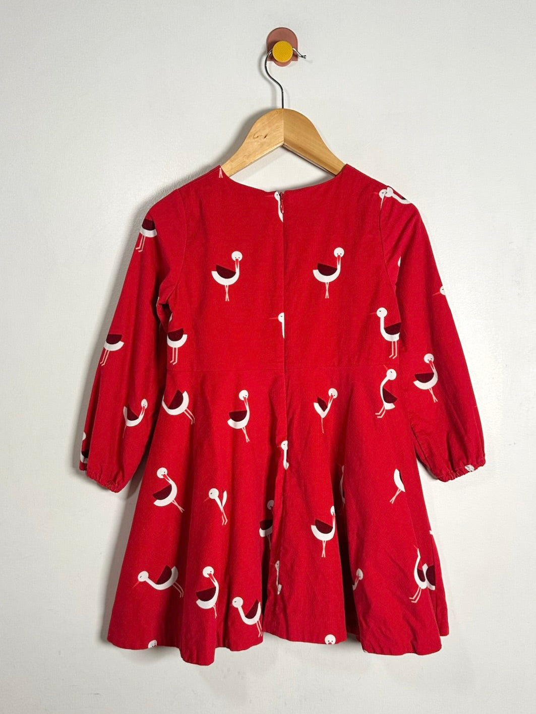 A red long-sleeve dress with a white and black bird print, hanging on a wooden hanger against a plain light gray wall.