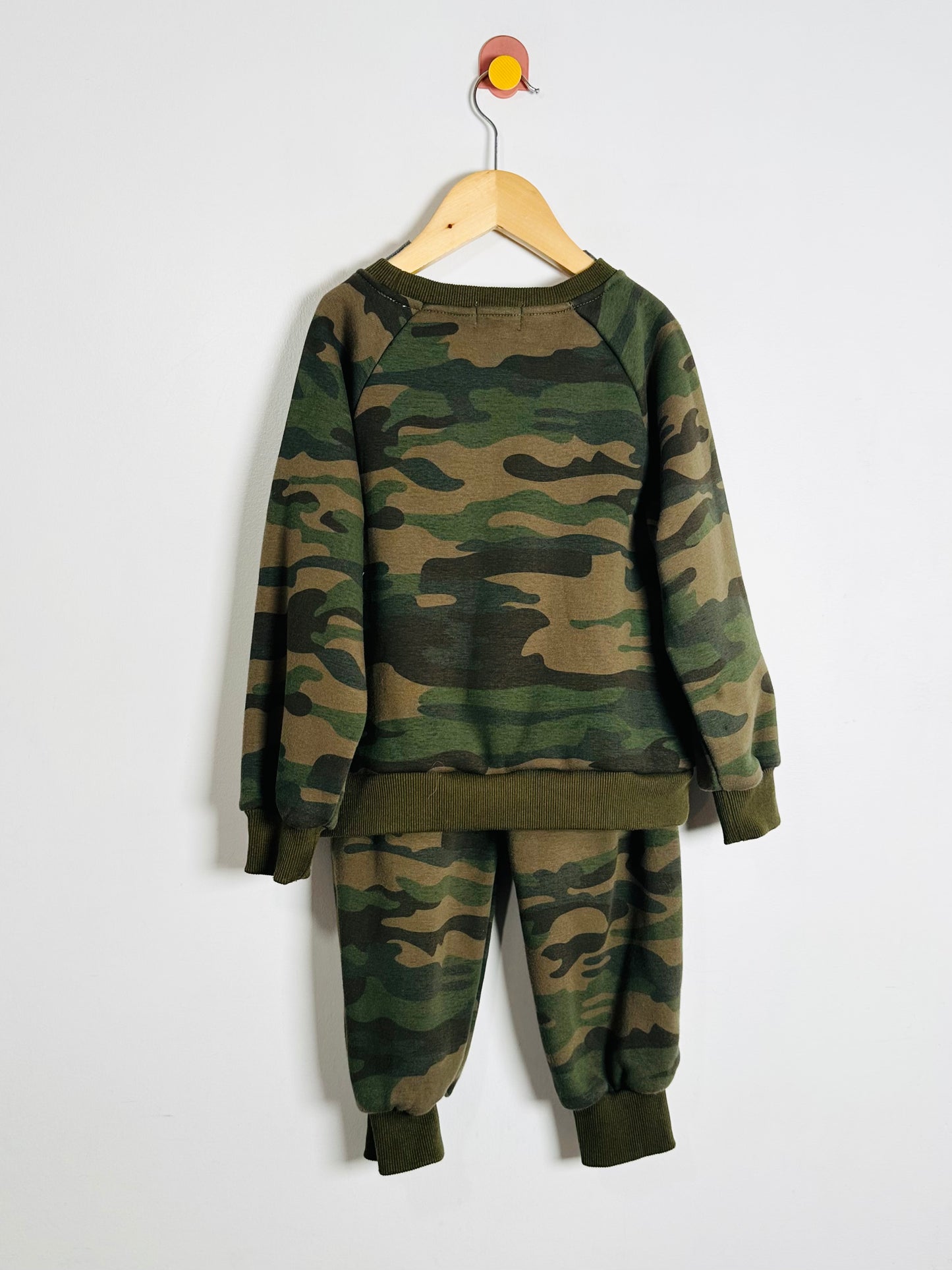Camouflage sweatshirt and pants set on a hanger against a white background