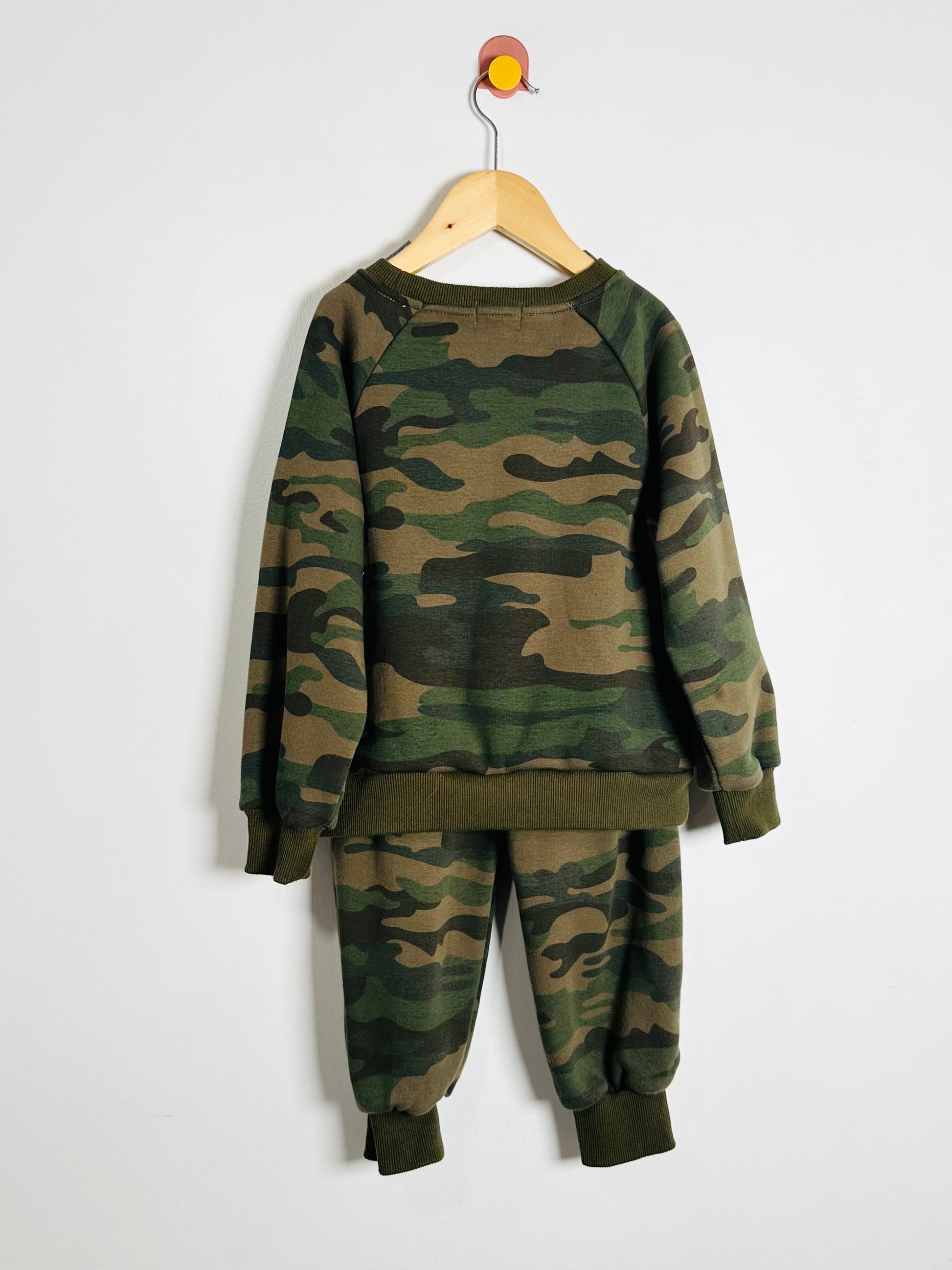 Camouflage sweatshirt and pants set on a hanger against a white background