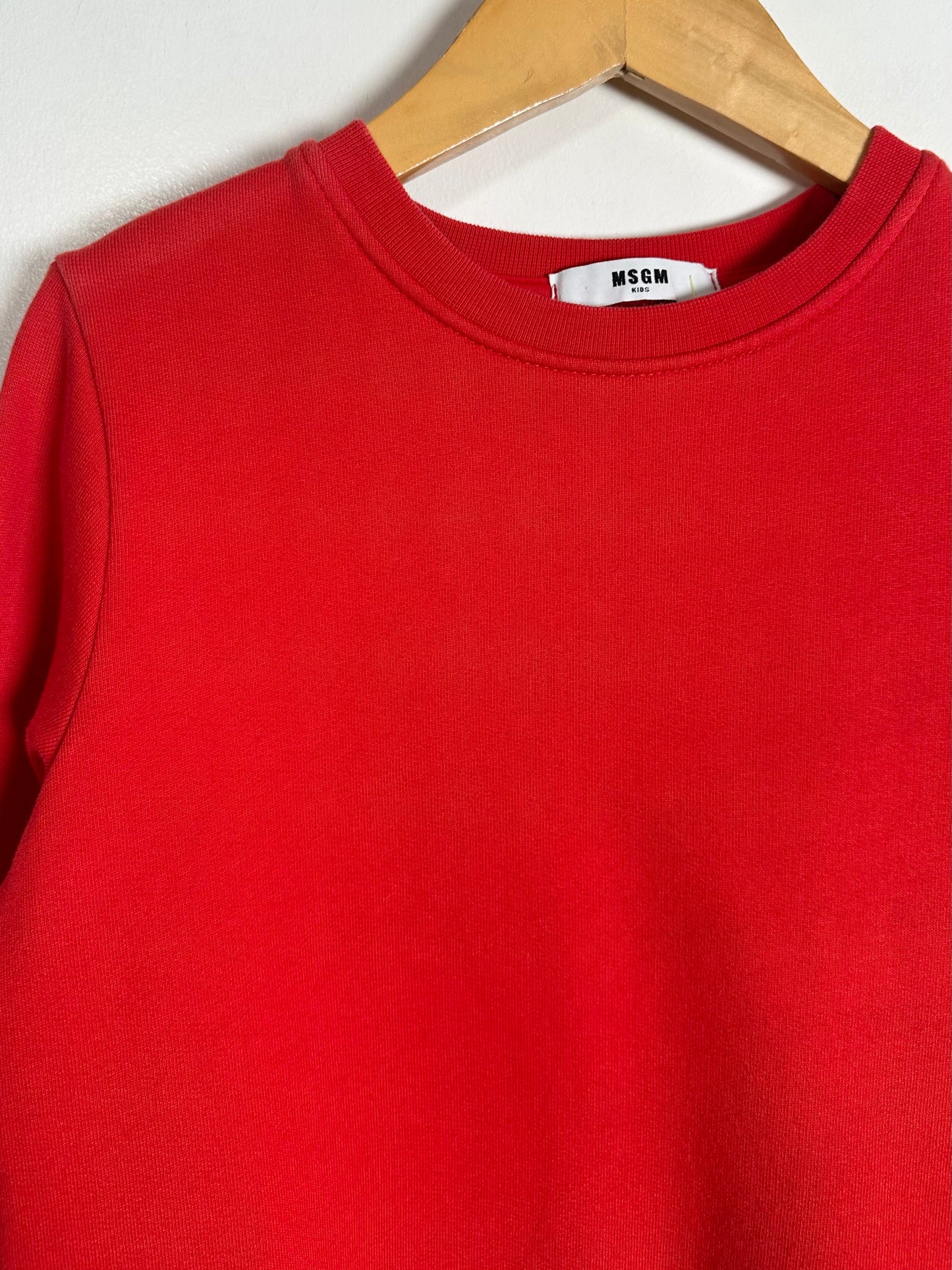 Red sweatshirt with a visible brand label on a wooden hanger against a white background