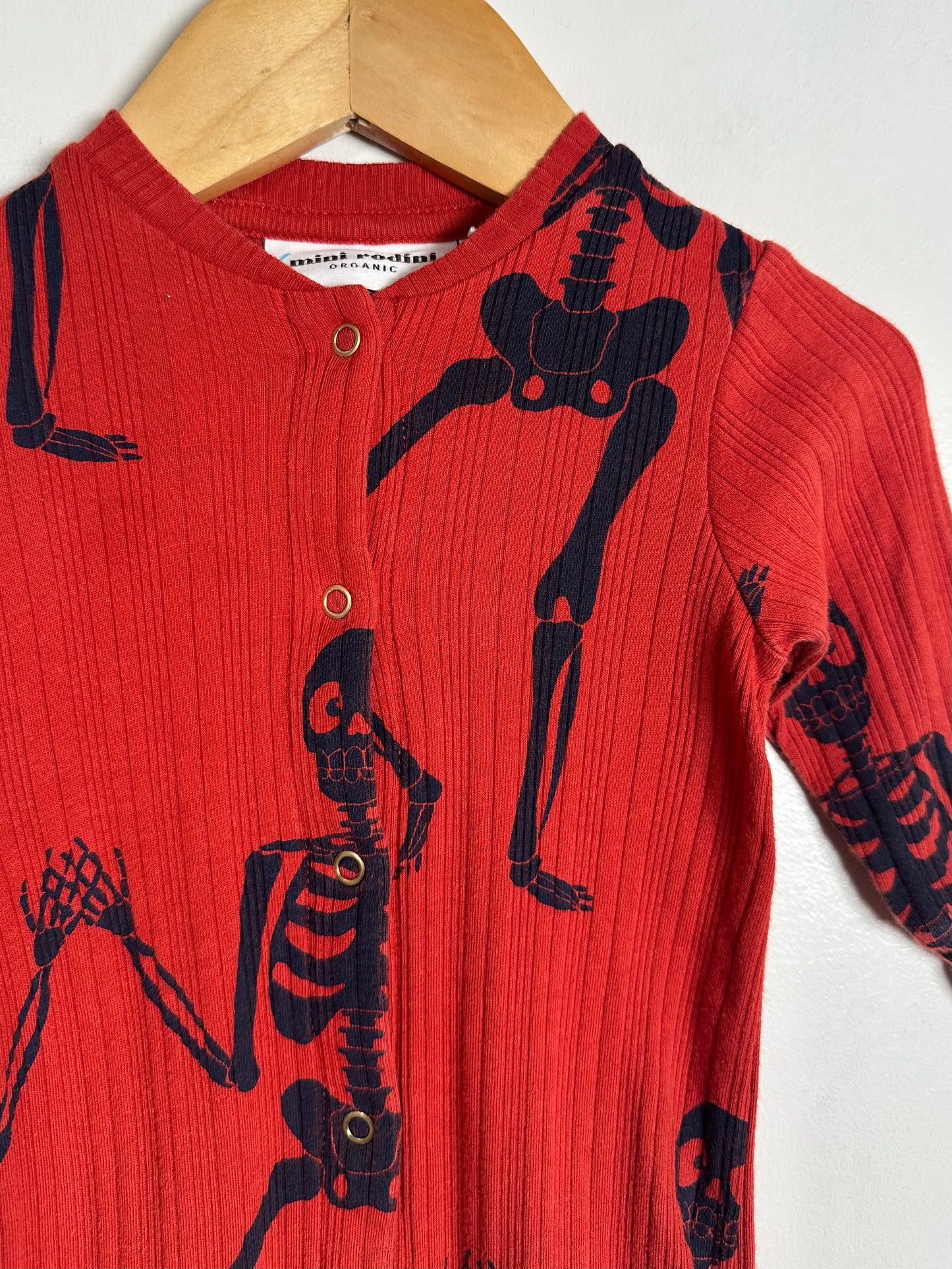 Red shirt with black skeleton designs on a wooden hanger against a white background
