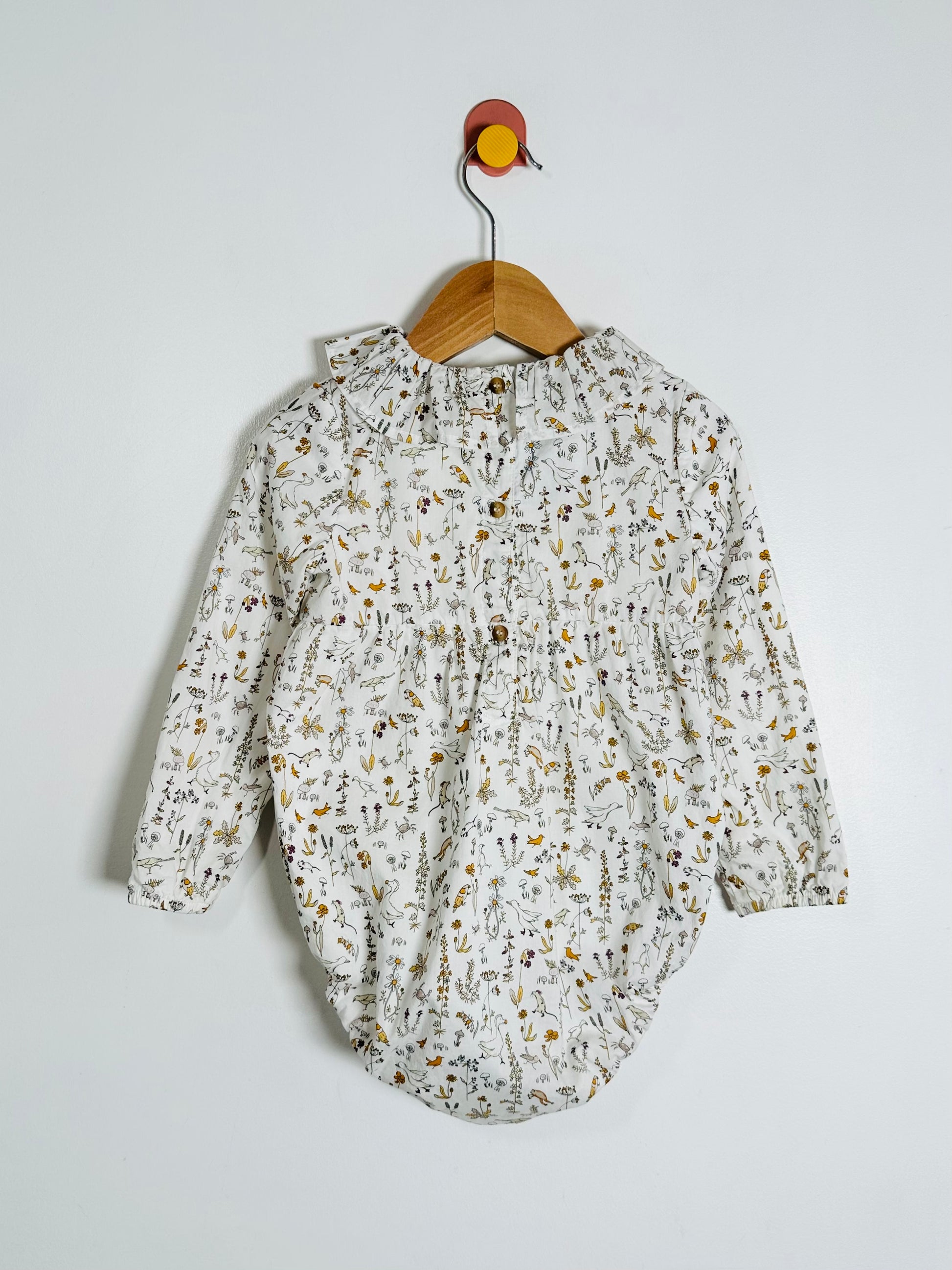 Floral baby romper on a hanger against a white background
