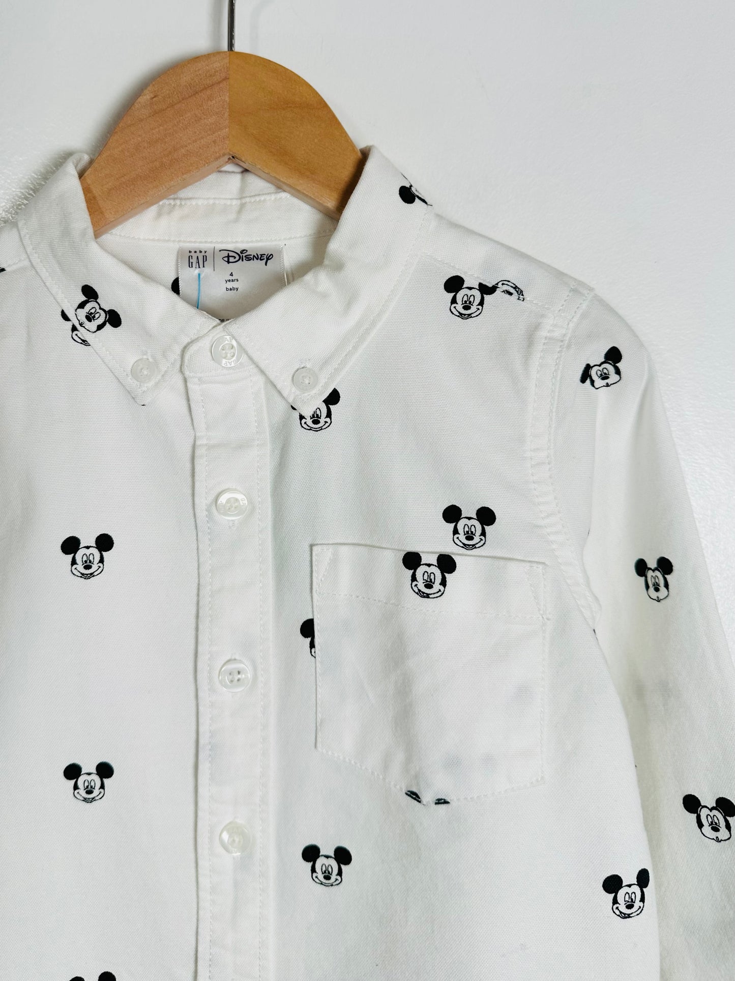 White shirt with black Mickey Mouse icons on a wooden hanger against a white background