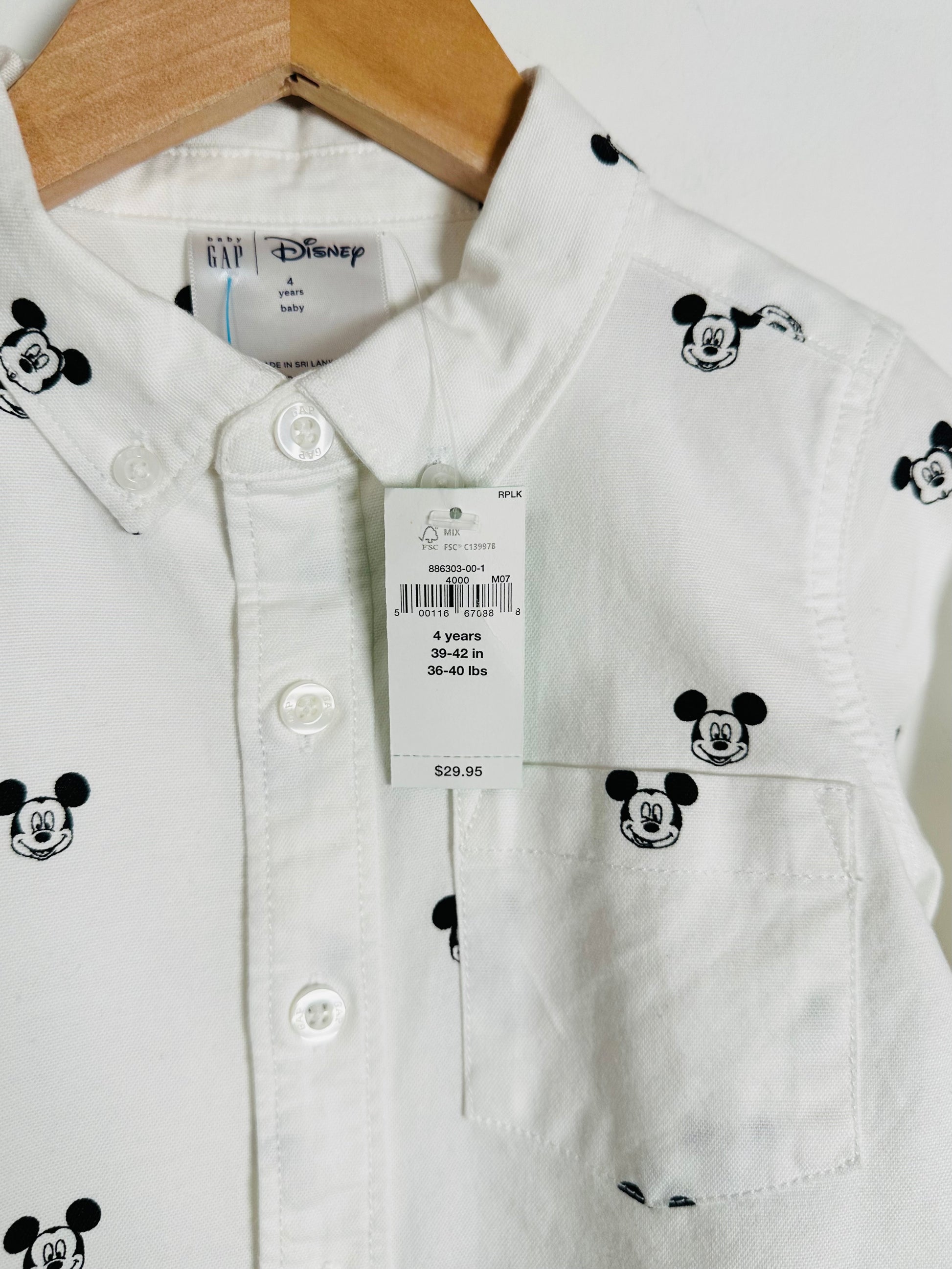White shirt with black Mickey Mouse patterns on a hanger, with a visible tag.