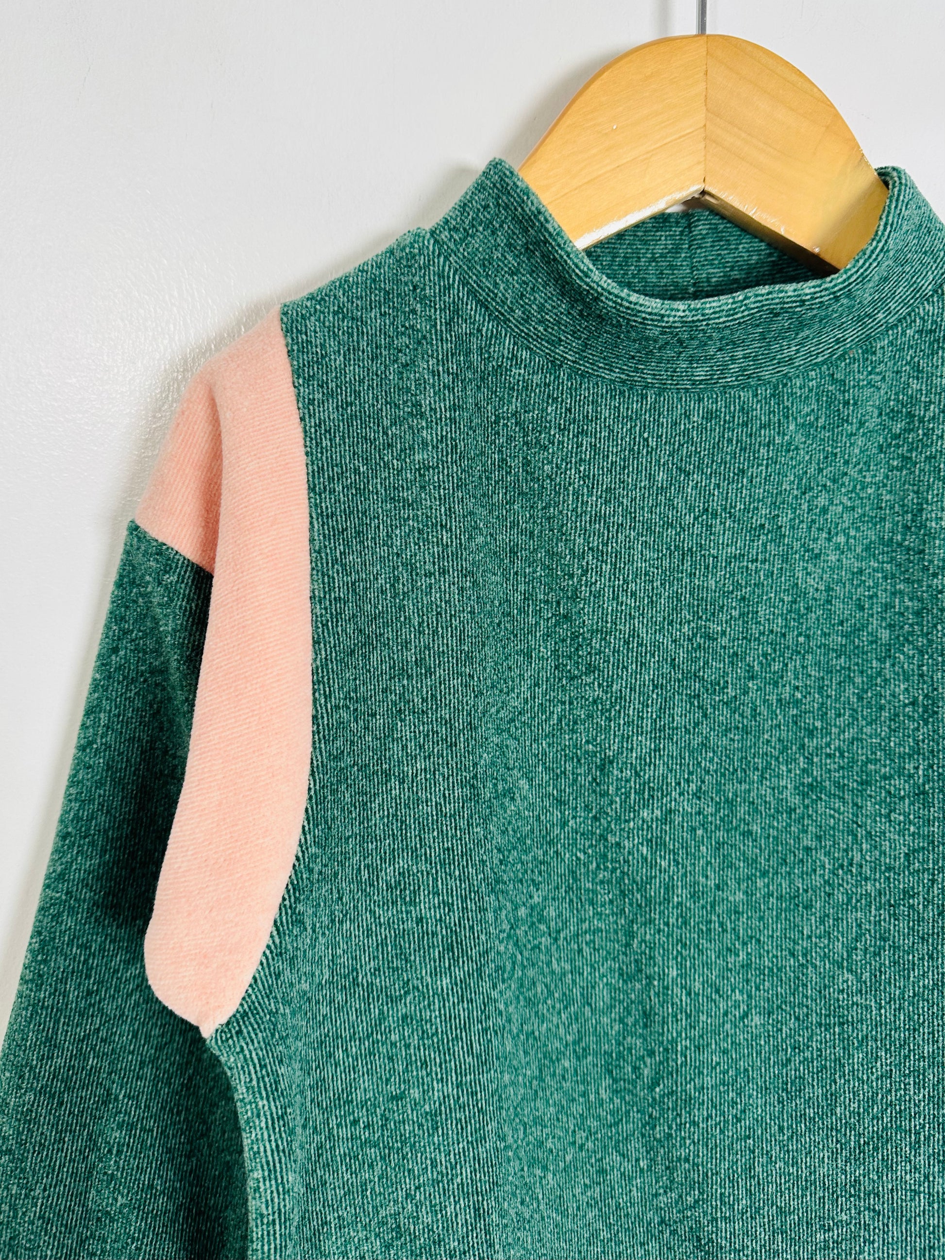 Green sweater with pink sleeves on a wooden hanger against a white background