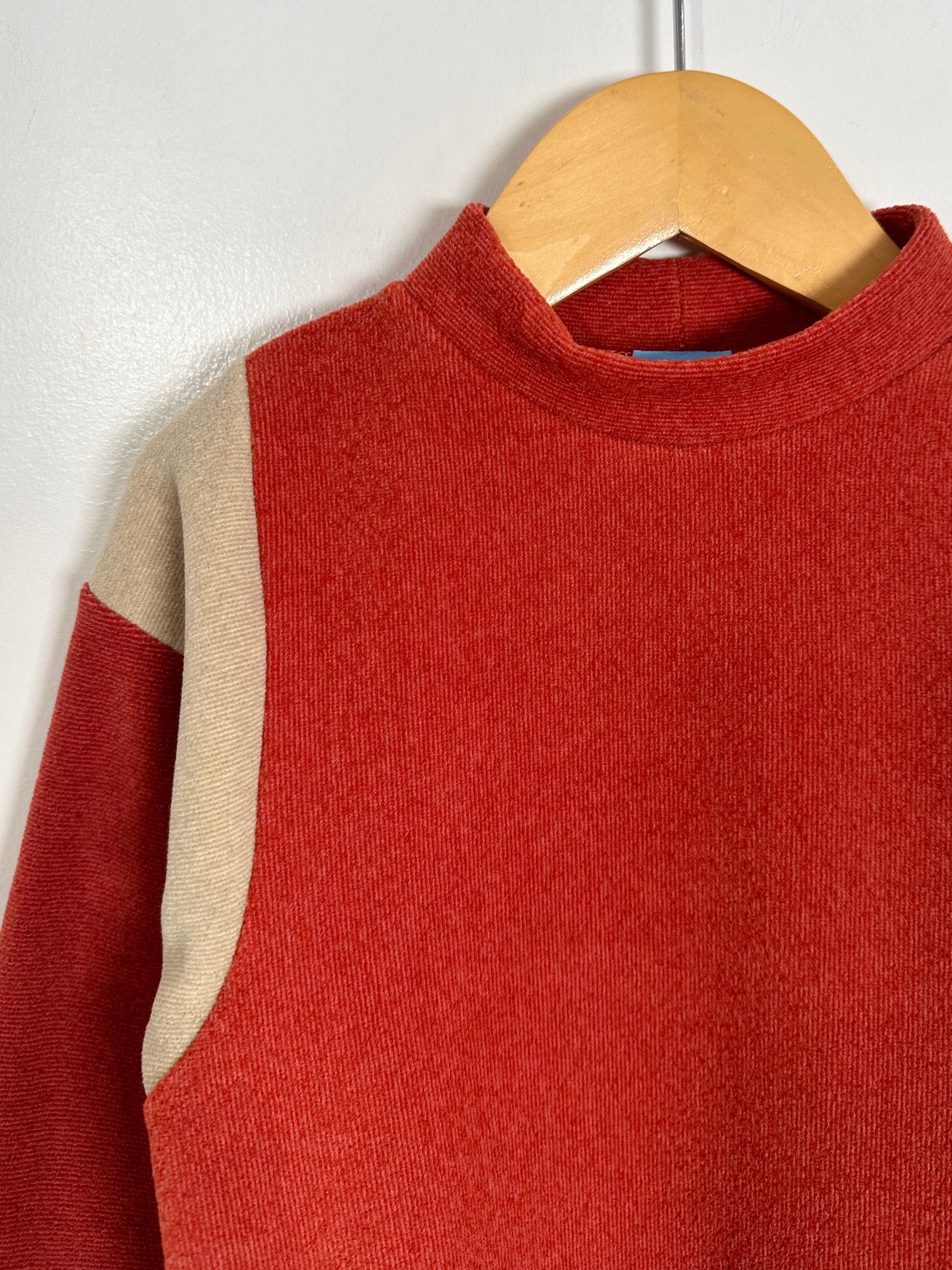 Red sweater with beige sleeves on a wooden hanger against a white wall
