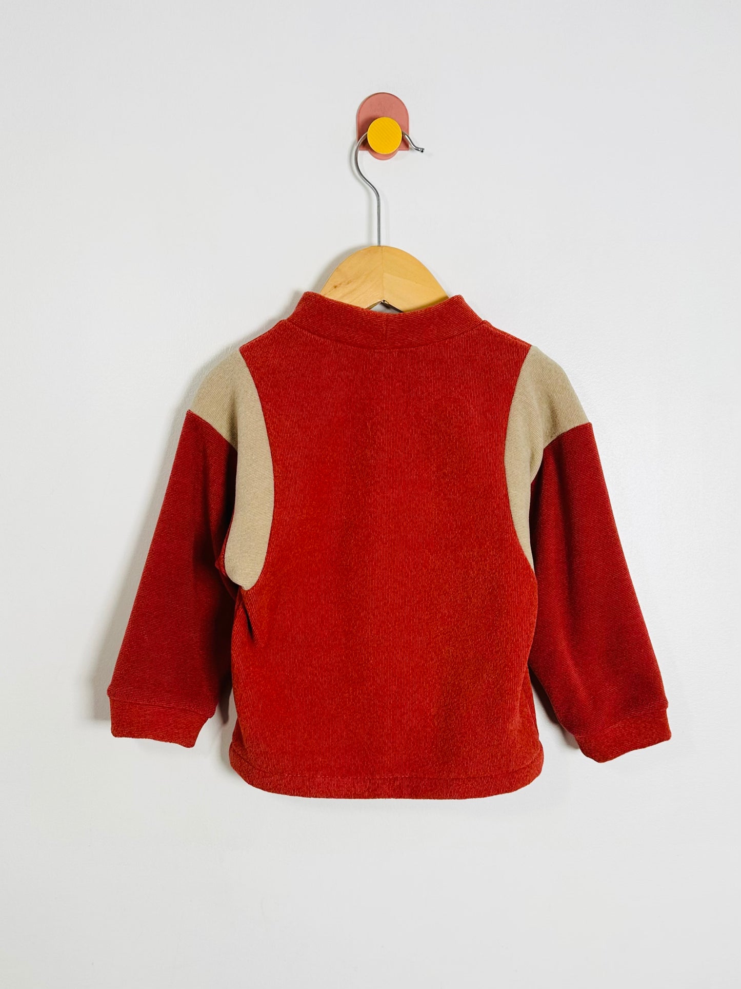 Red and beige children's sweater on a hanger against a white background