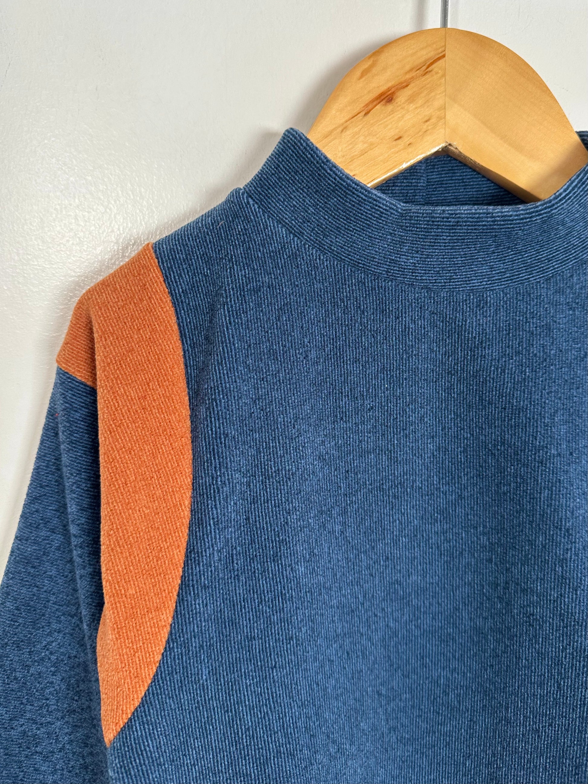Blue sweater with orange accents on a wooden hanger against a white wall