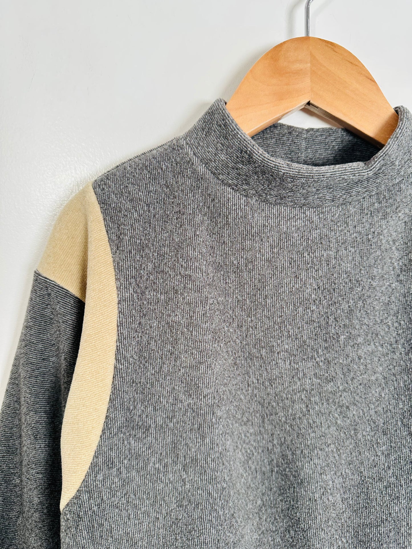 Gray sweater with beige accents on a wooden hanger against a white background