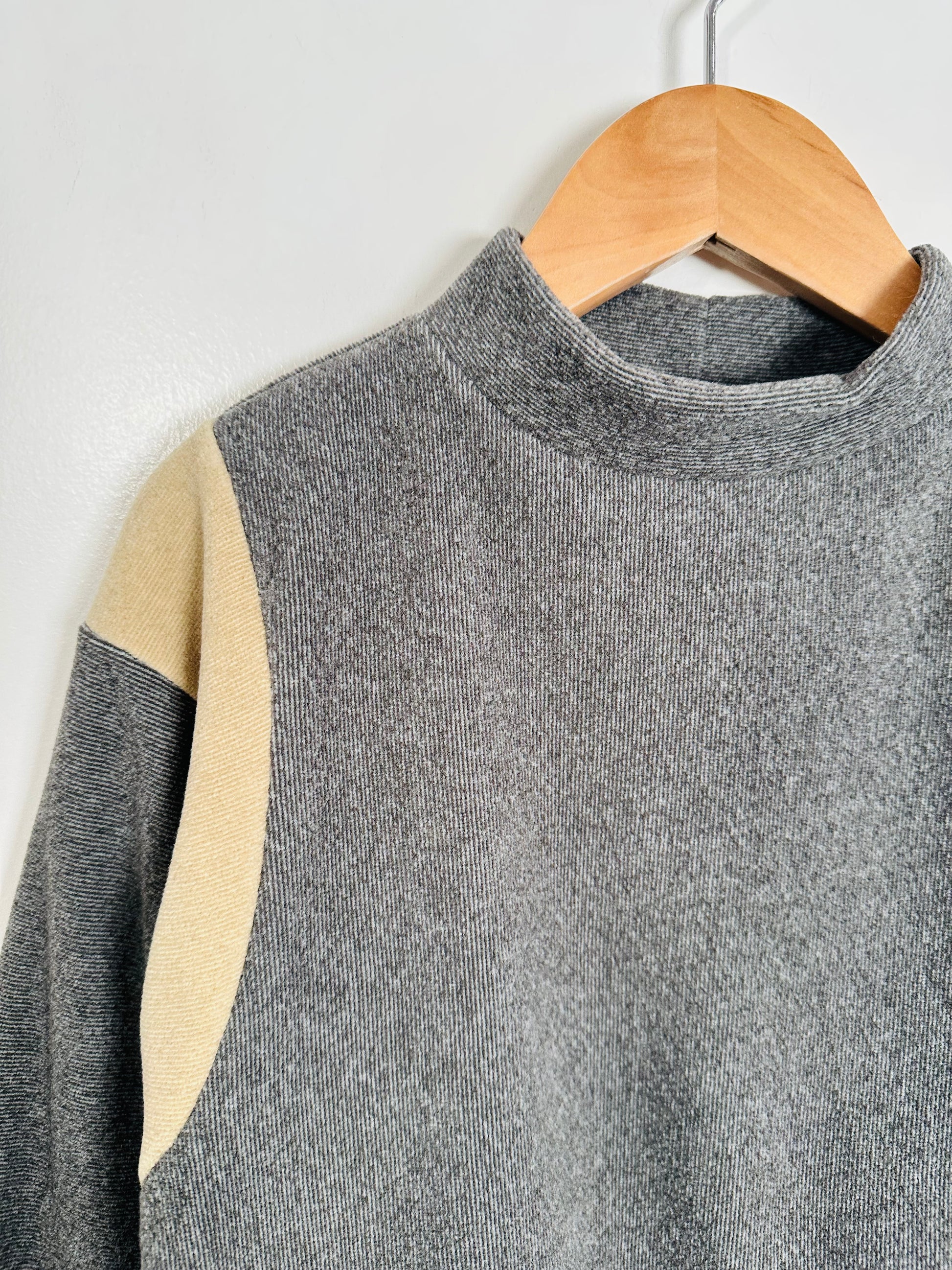 Gray sweater with beige accents on a wooden hanger against a white background