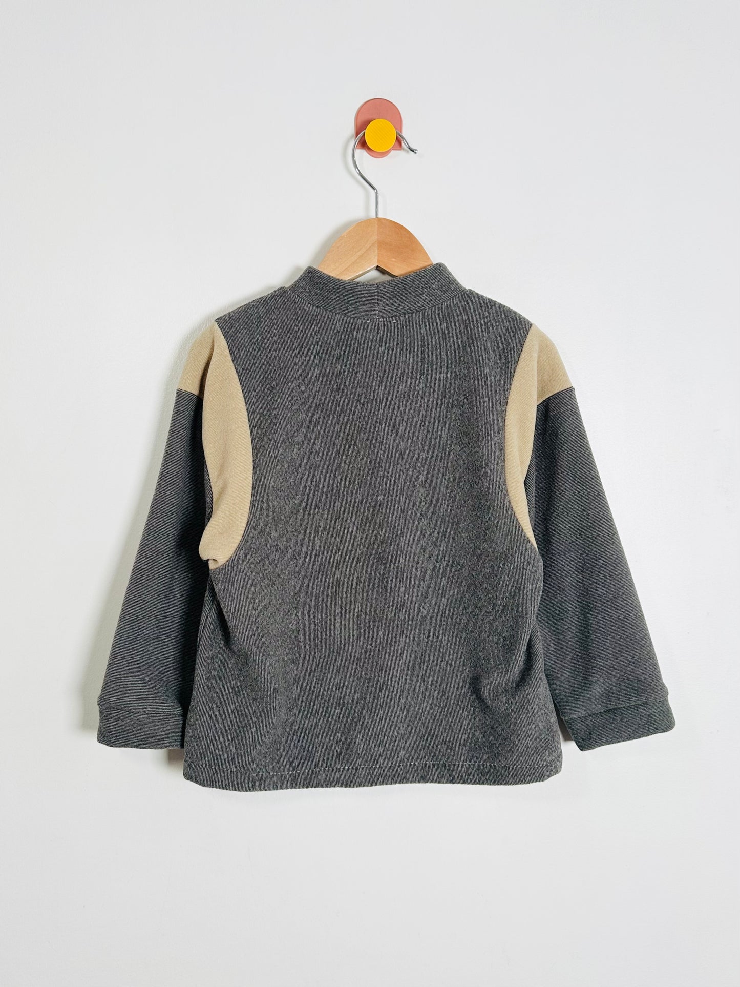 Gray fleece sweater with beige sleeves on a hanger against a white background