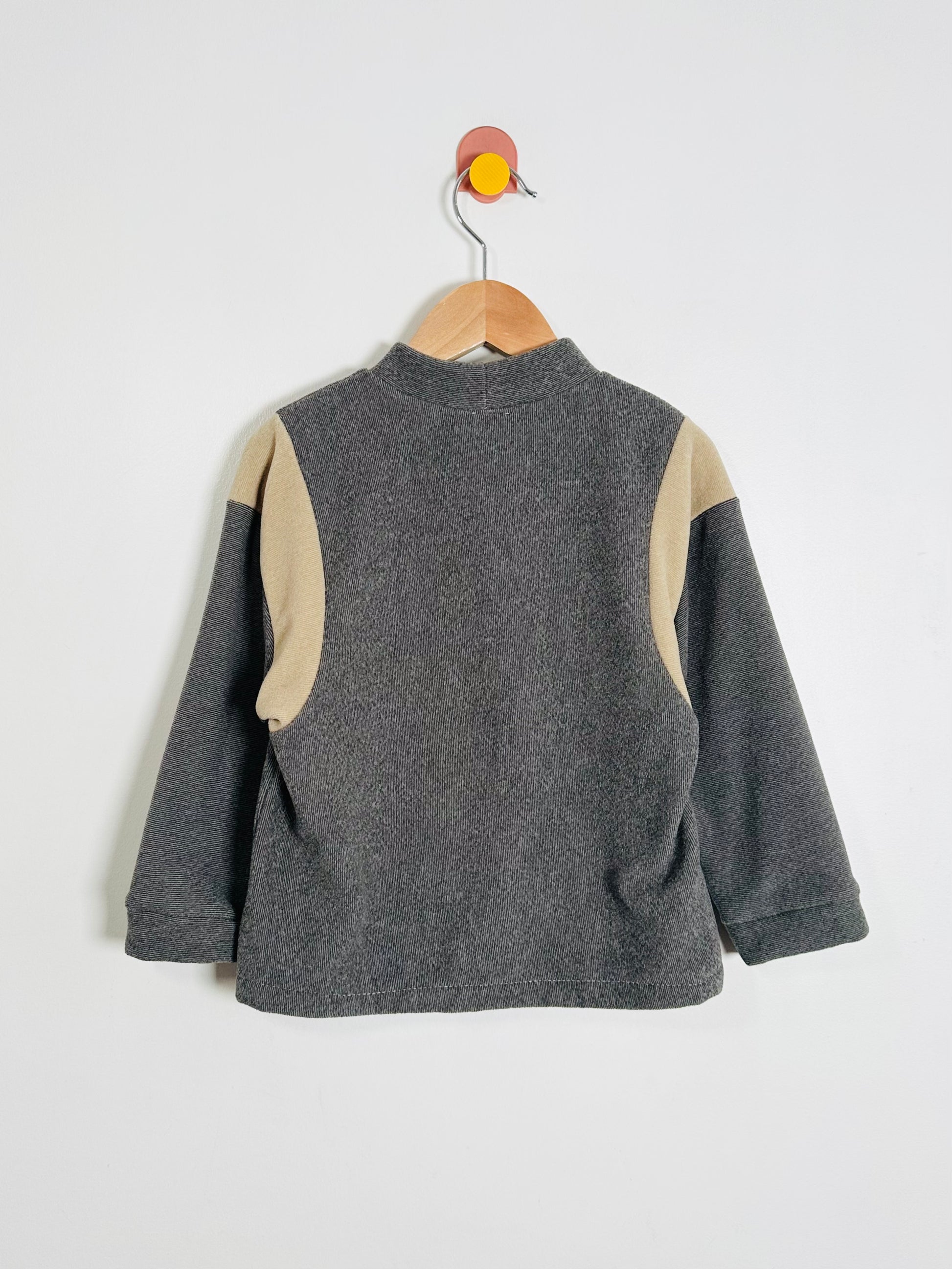 Gray fleece sweater with beige sleeves on a hanger against a white background