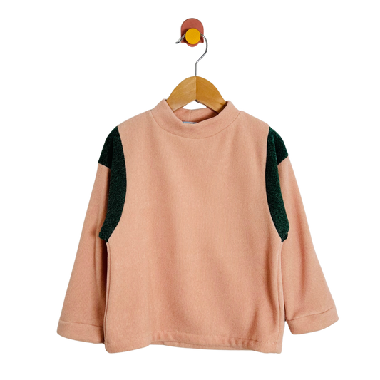 Pink sweater with green sleeves on a wooden hanger against a white background