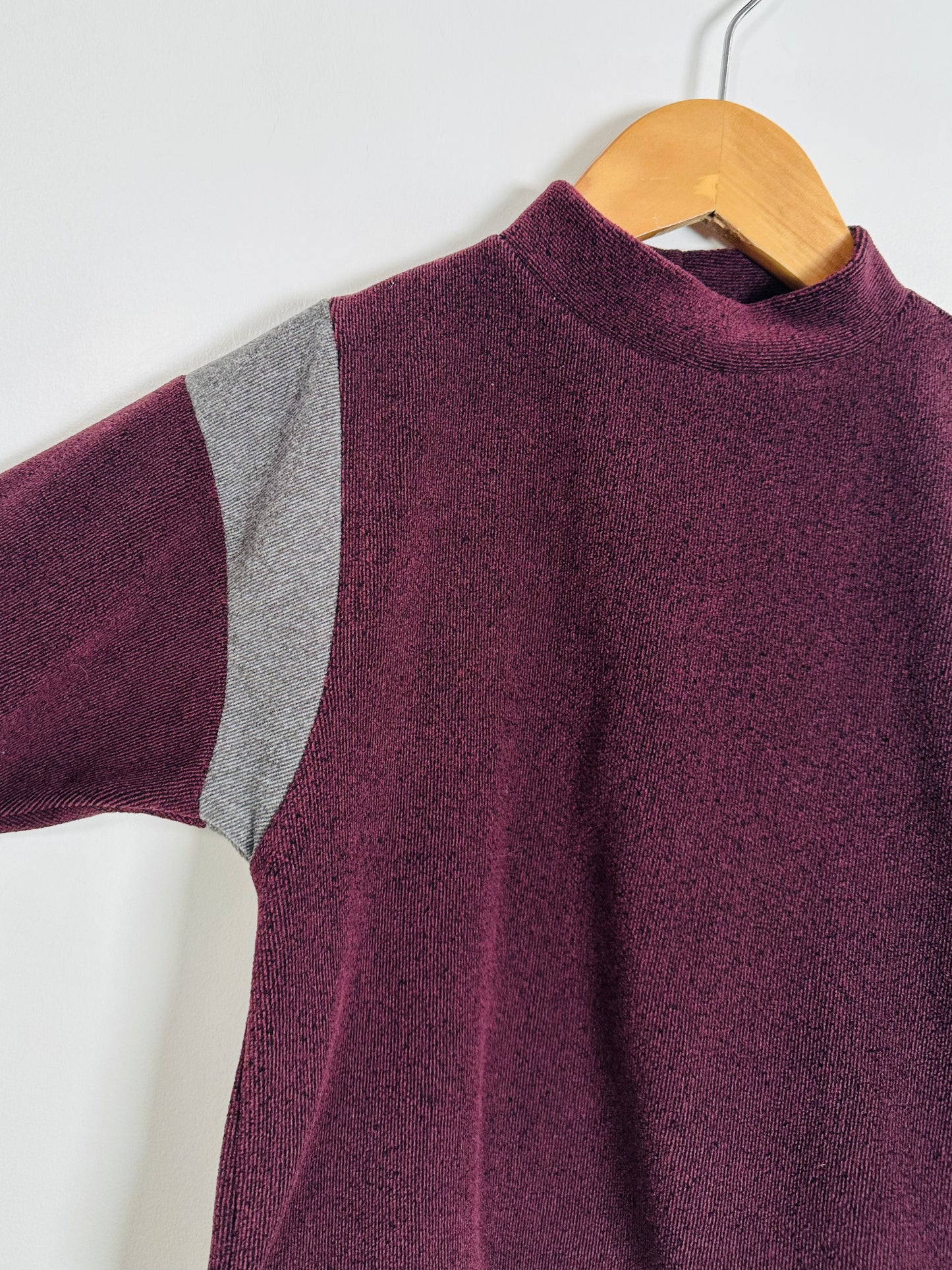Purple sweater with gray shoulder detail on a wooden hanger against a white background