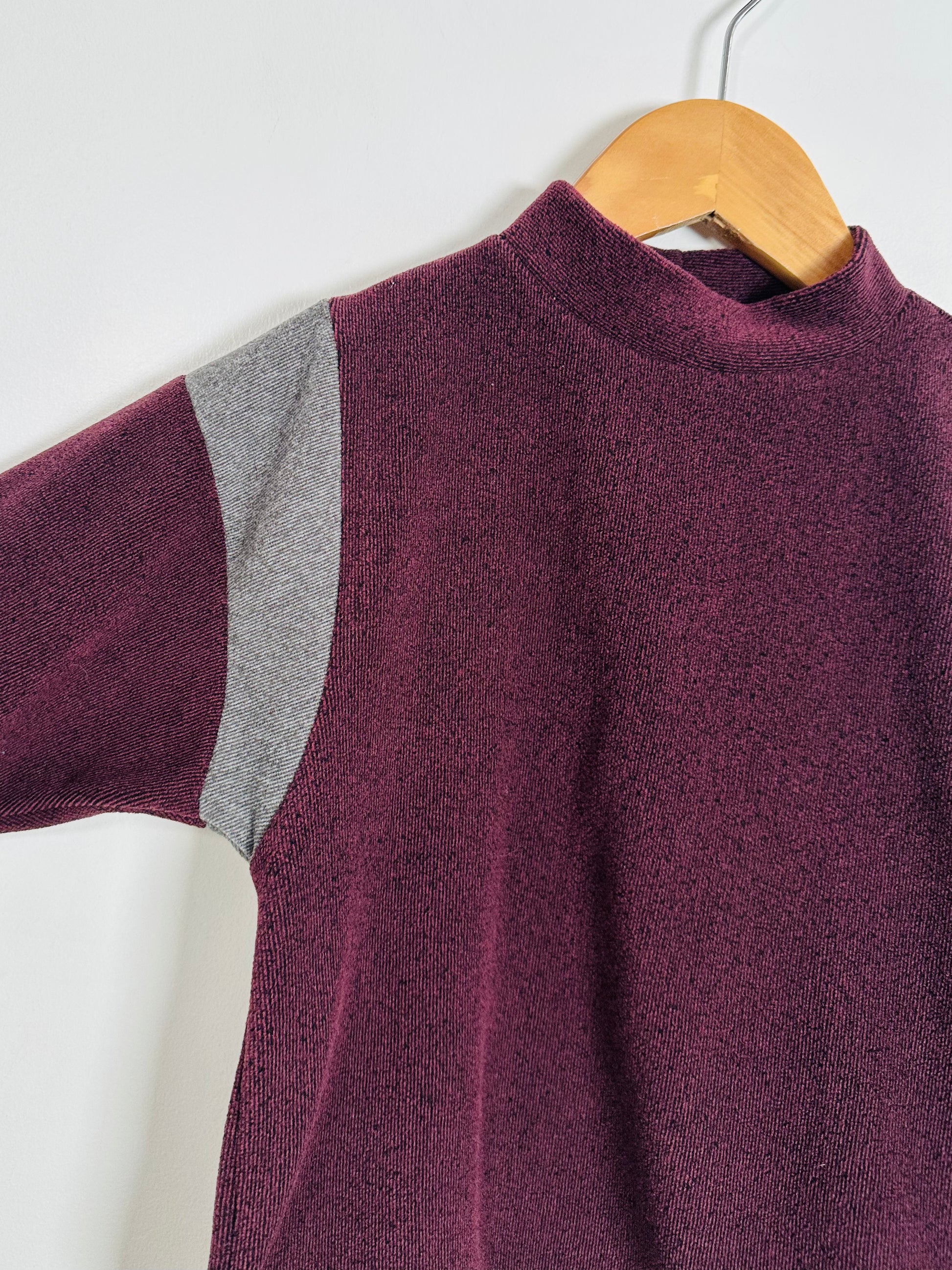 Purple sweater with gray shoulder detail on a wooden hanger against a white background