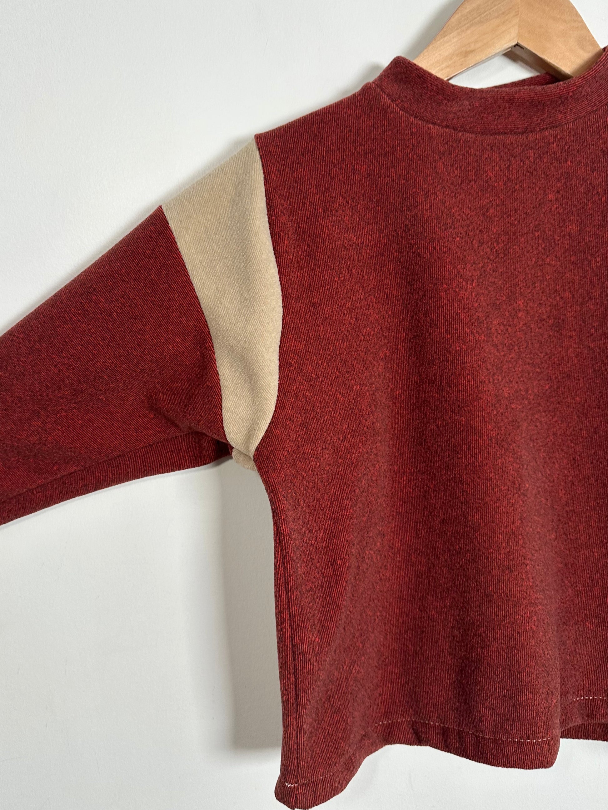 Red sweater with beige sleeves on a hanger against a white background