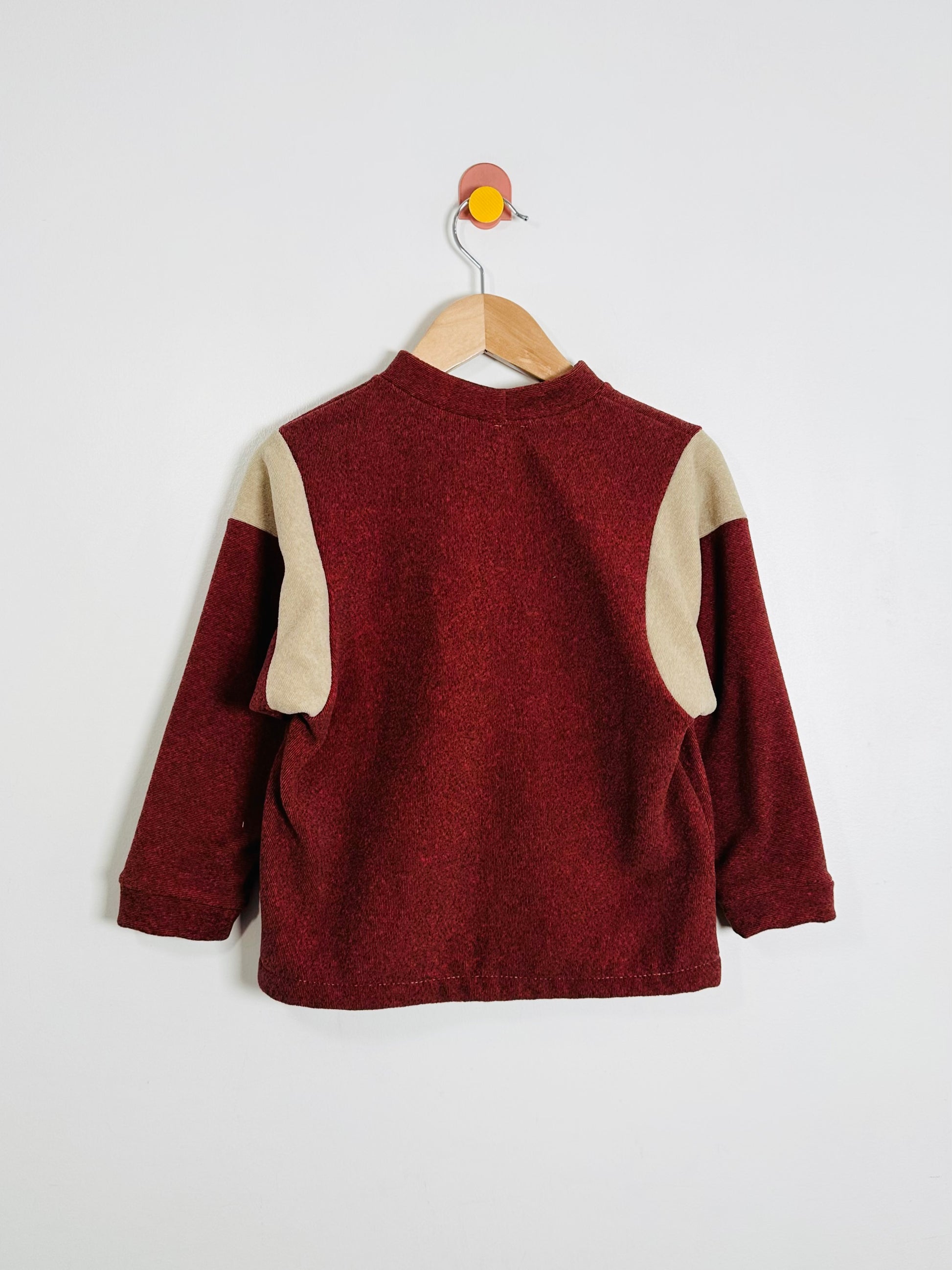 Maroon sweater with beige sleeves on a hanger against a white background