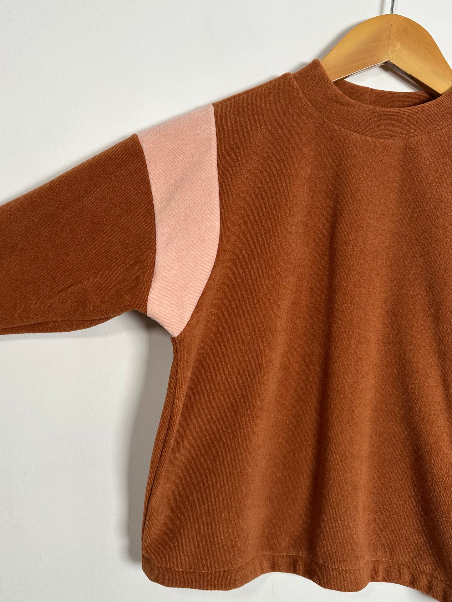 Brown sweater with pink accents on a wooden hanger against a white background