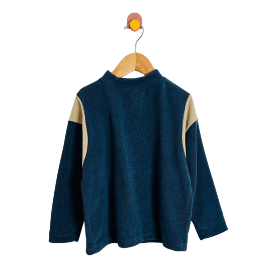 Blue sweater with beige sleeves on a wooden hanger against a white background