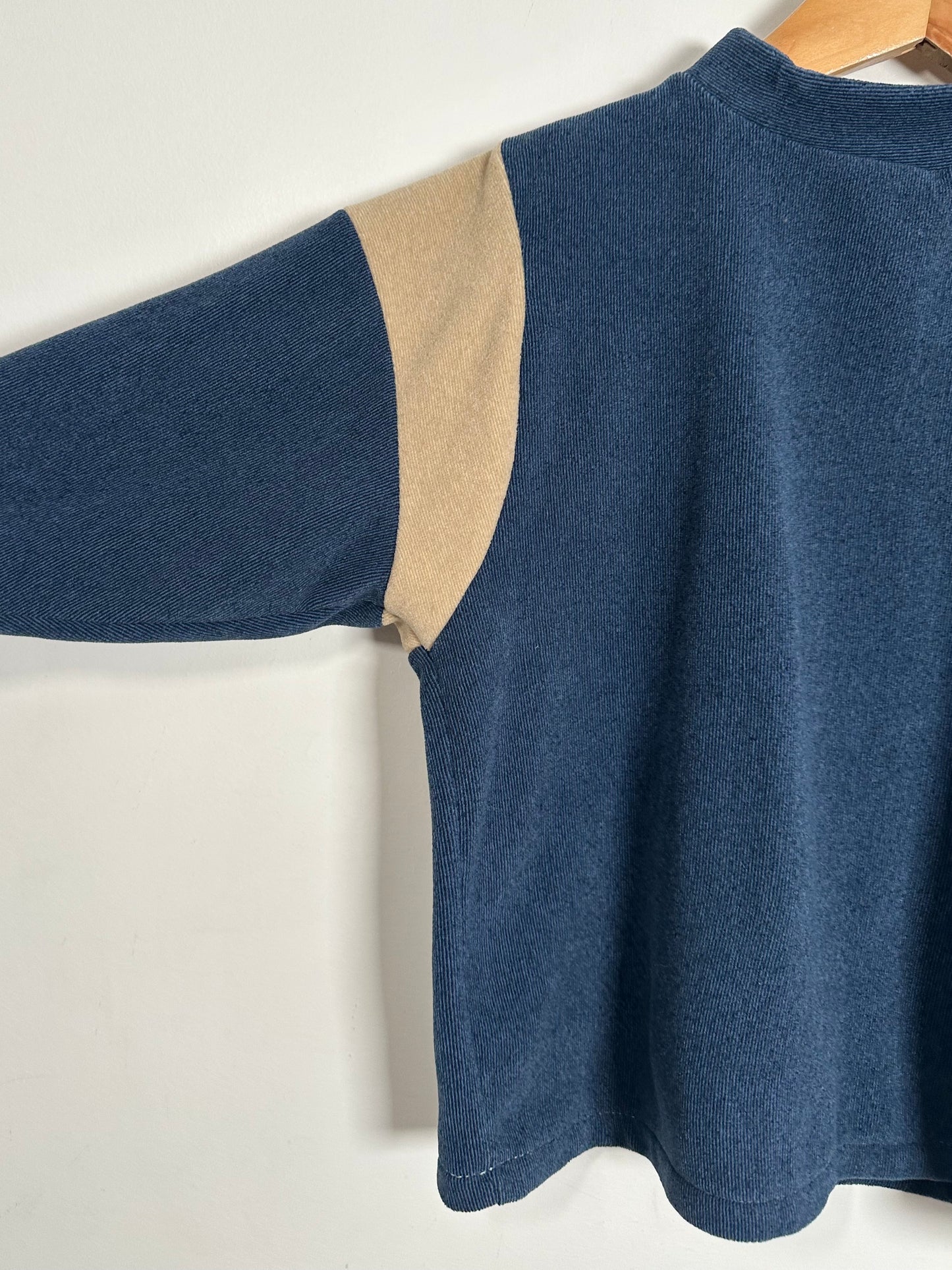 Blue sweater with beige accents on a hanger against a white background