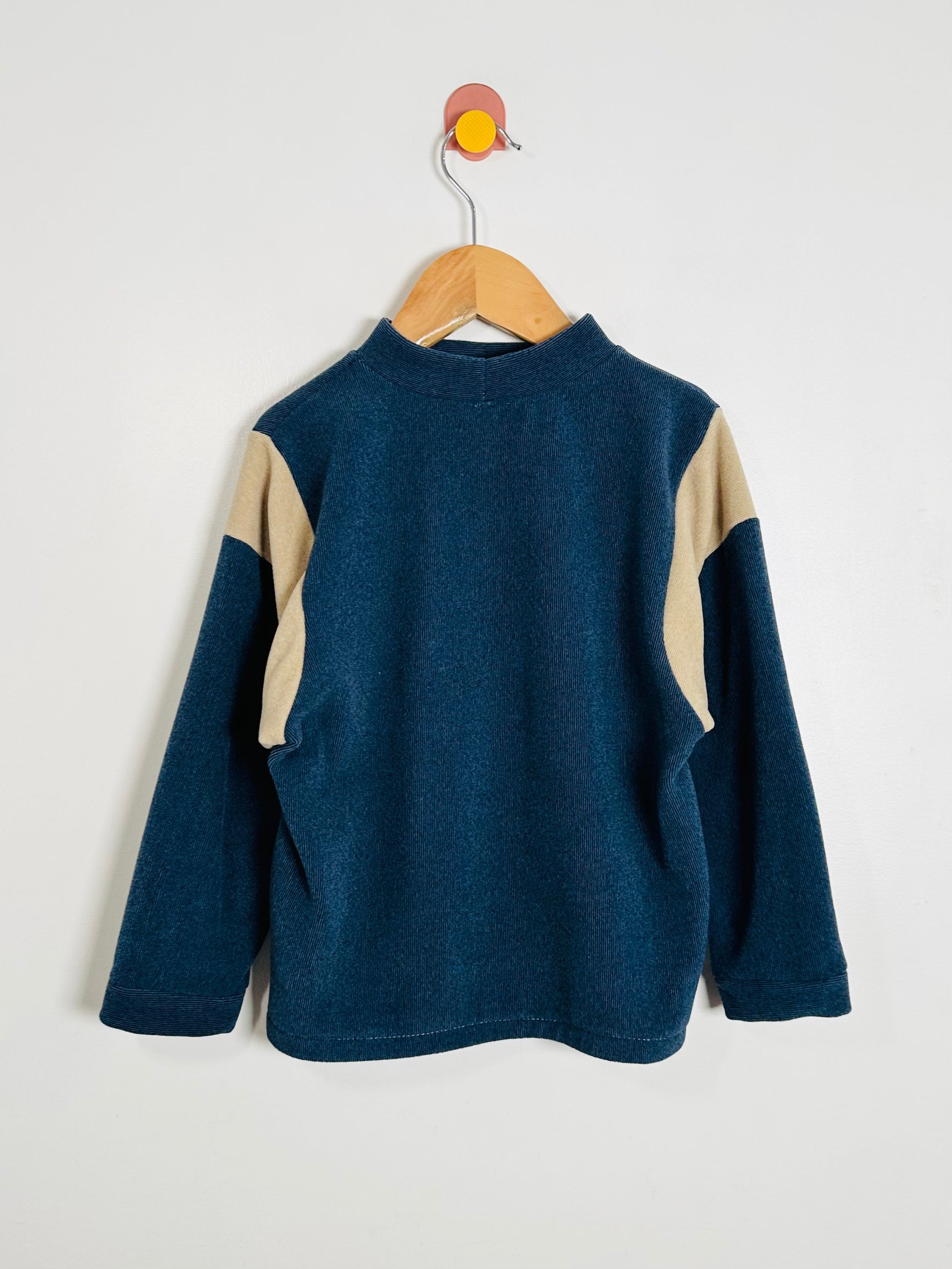 Blue and beige fleece pullover on a wooden hanger against a white background