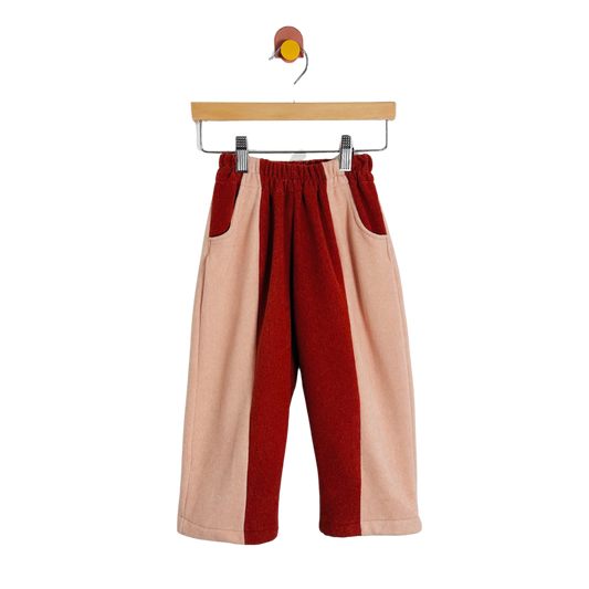 Color-blocked pants with red and beige sections on a hanger against a white background