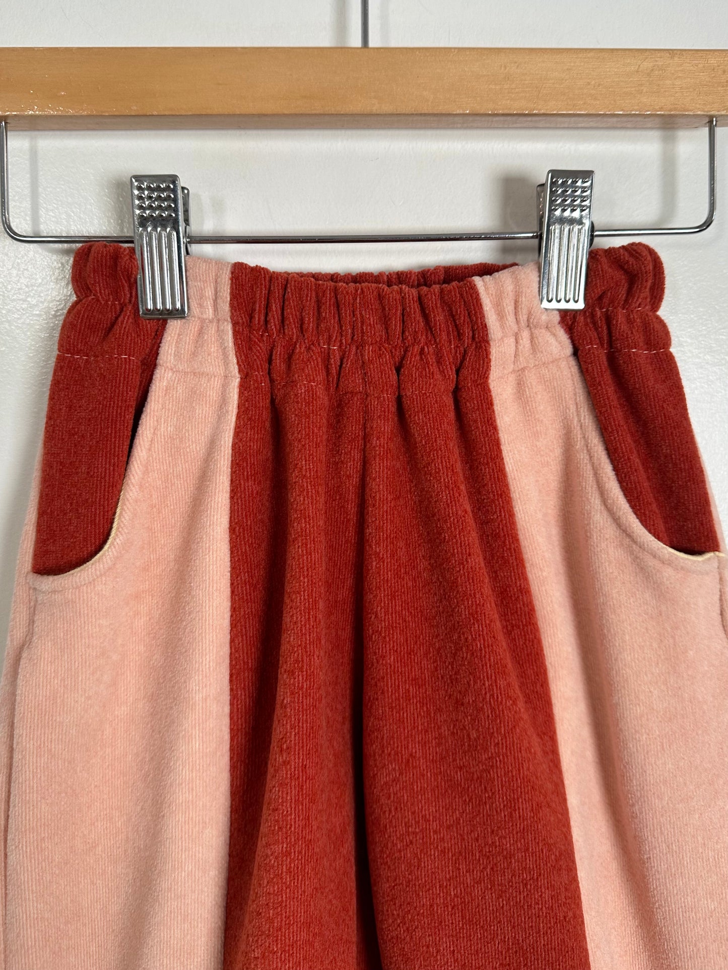 Color-blocked pants with rust and pink sections hanging on a rack.