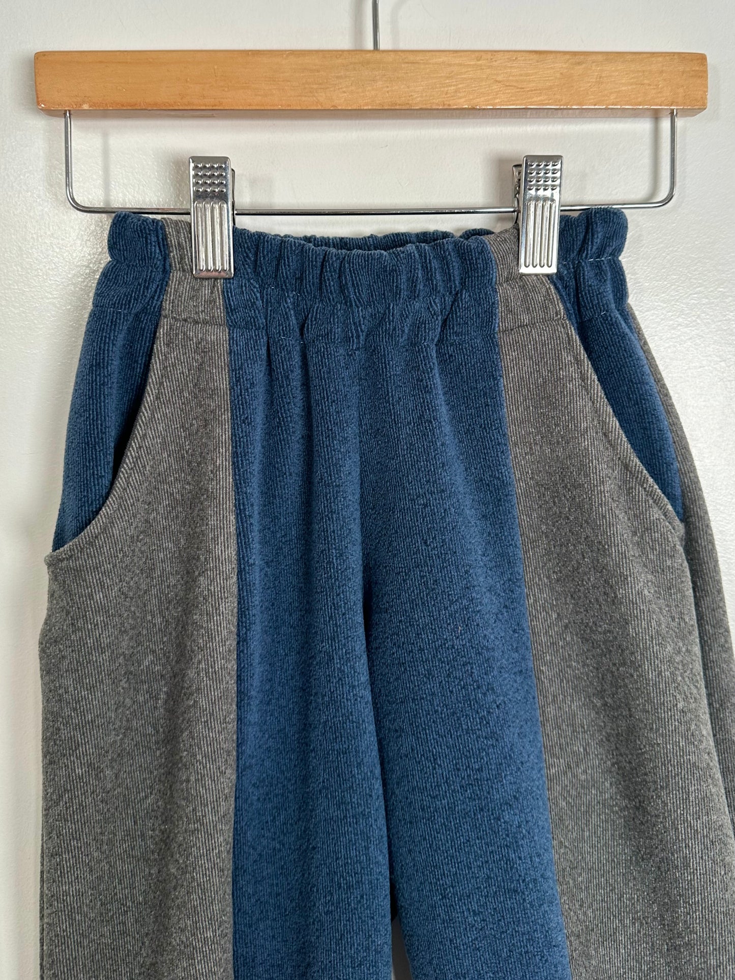 Gray and blue pants hanging on a wooden hanger against a white background