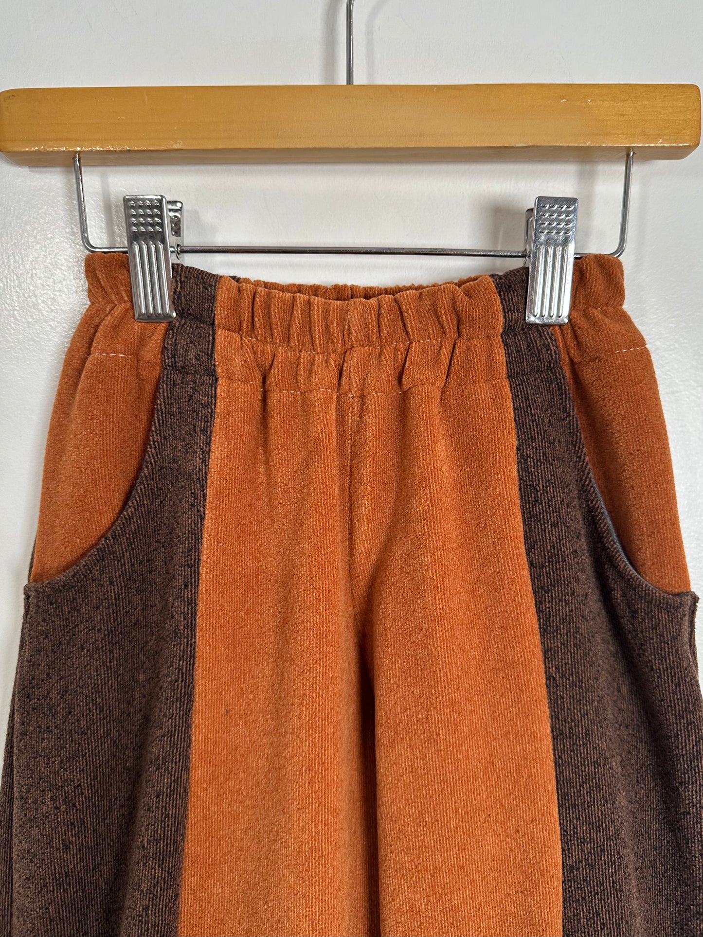Brown and orange pants on a hanger against a white wall