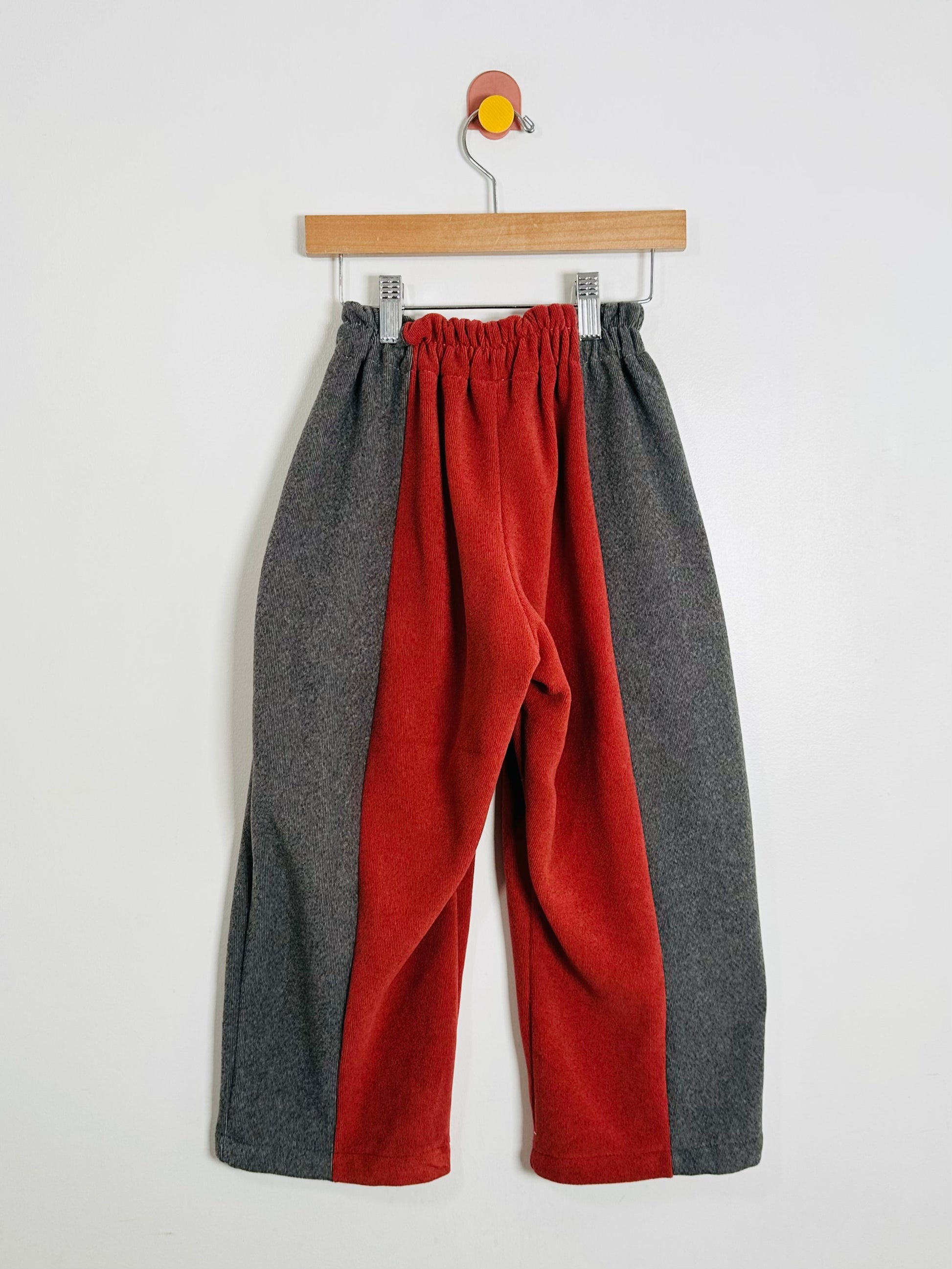 Color-blocked pants with gray and red sections on a hanger against a white background