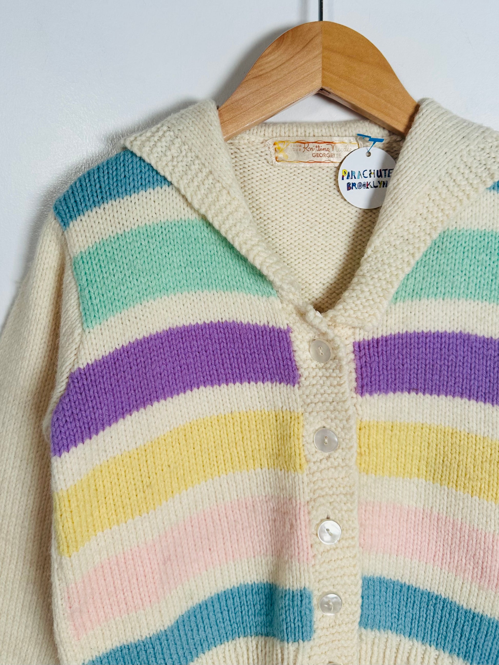 Pastel striped cardigan on a hanger against a white background