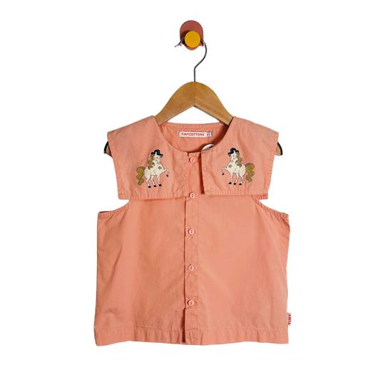 Pink sleeveless shirt with horse designs on a hanger against a white background