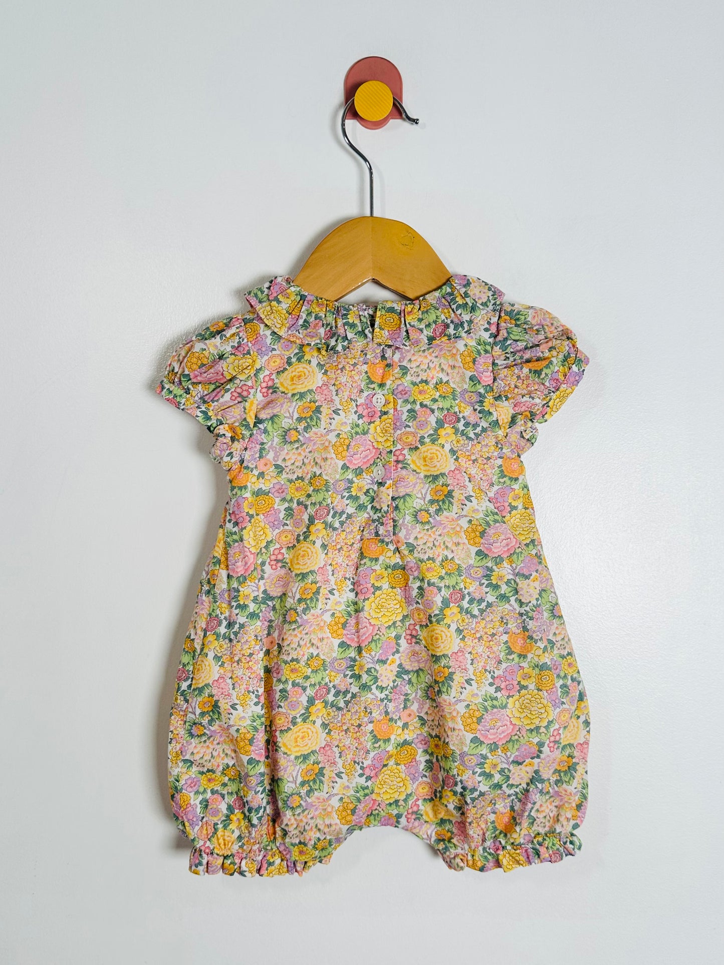 Floral baby romper on a hanger against a white background