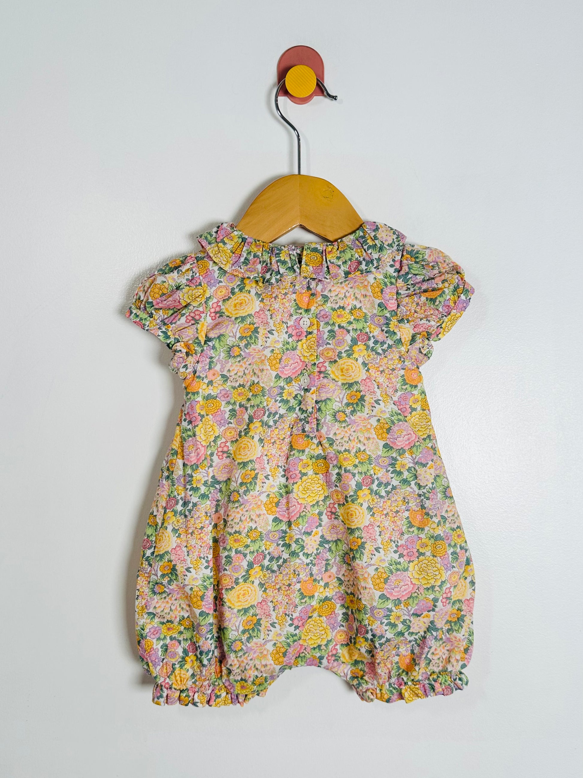 Floral baby romper on a hanger against a white background