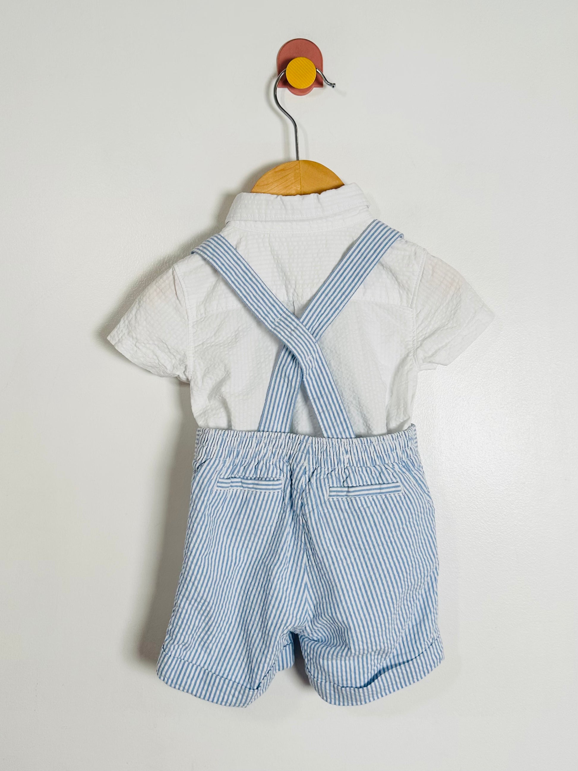 Children's outfit with white shirt and blue striped overalls on a hanger against a light background
